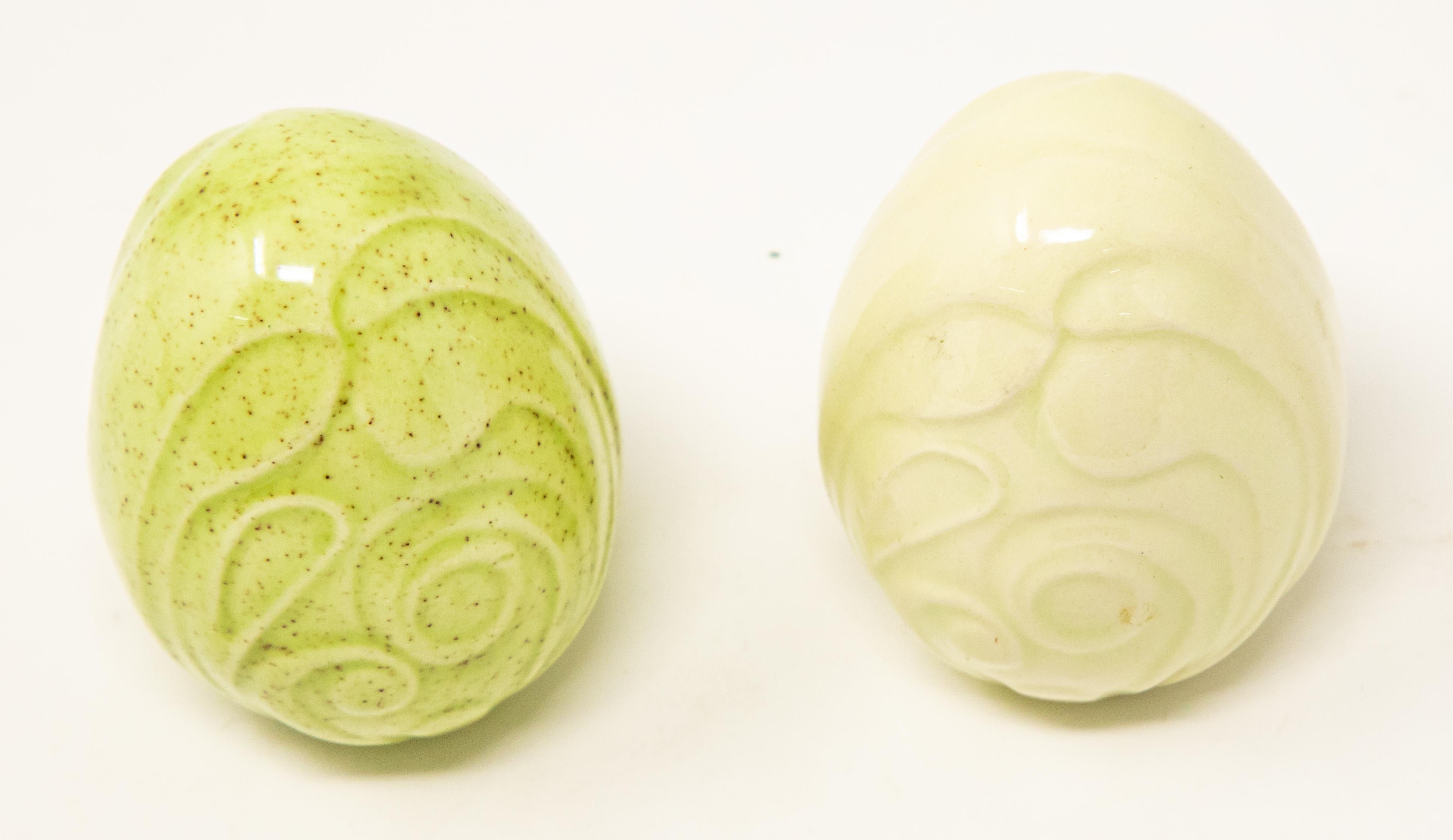 Offering a pair of ceramic glazed eggs. One is green with speckles and a swirled pattern. The other is solid cream with the same swirled pattern.