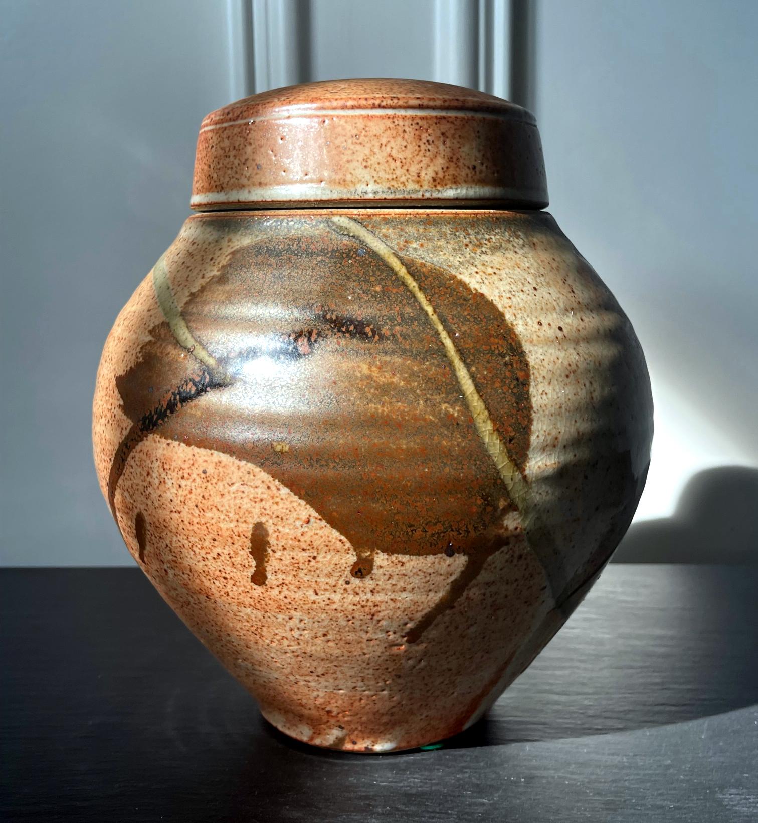 A ceramic (earth ware) lidded jar with glazed surface by American studio potter Karen Karnes (1925-2016). The mark on the jar indicates that the piece was made circa 2000s. The wheel-thrown piece shows off a beautiful form with a swell body and