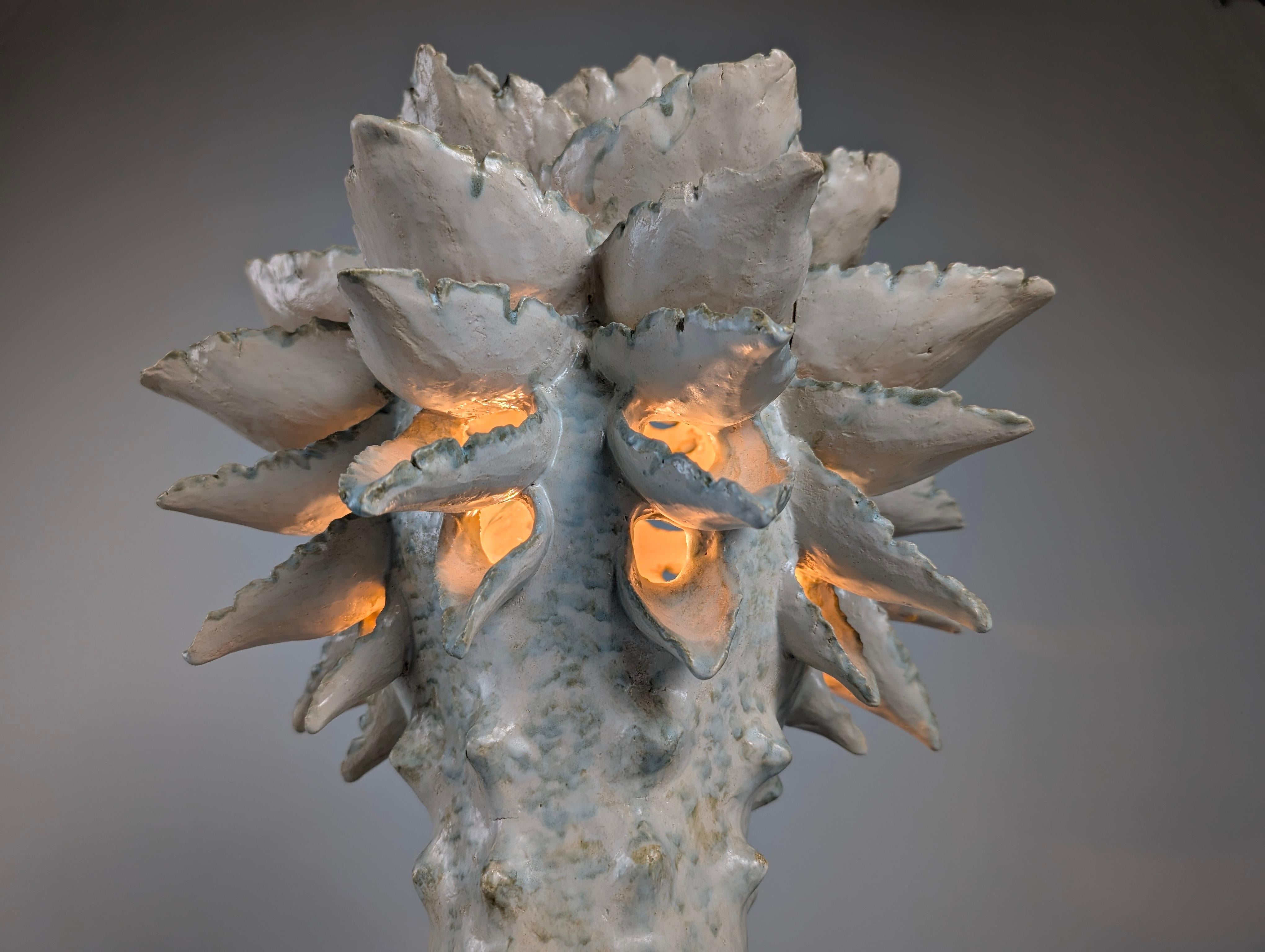 Expresiva escultura luminosa de la ceramista danesa Birthe Aksby, realizada en cerámica vidriada con diseños orgánicos inspirados en formas vegetales y corales marinos. La composición evoca el crecimiento natural, con volúmenes que emergen de una