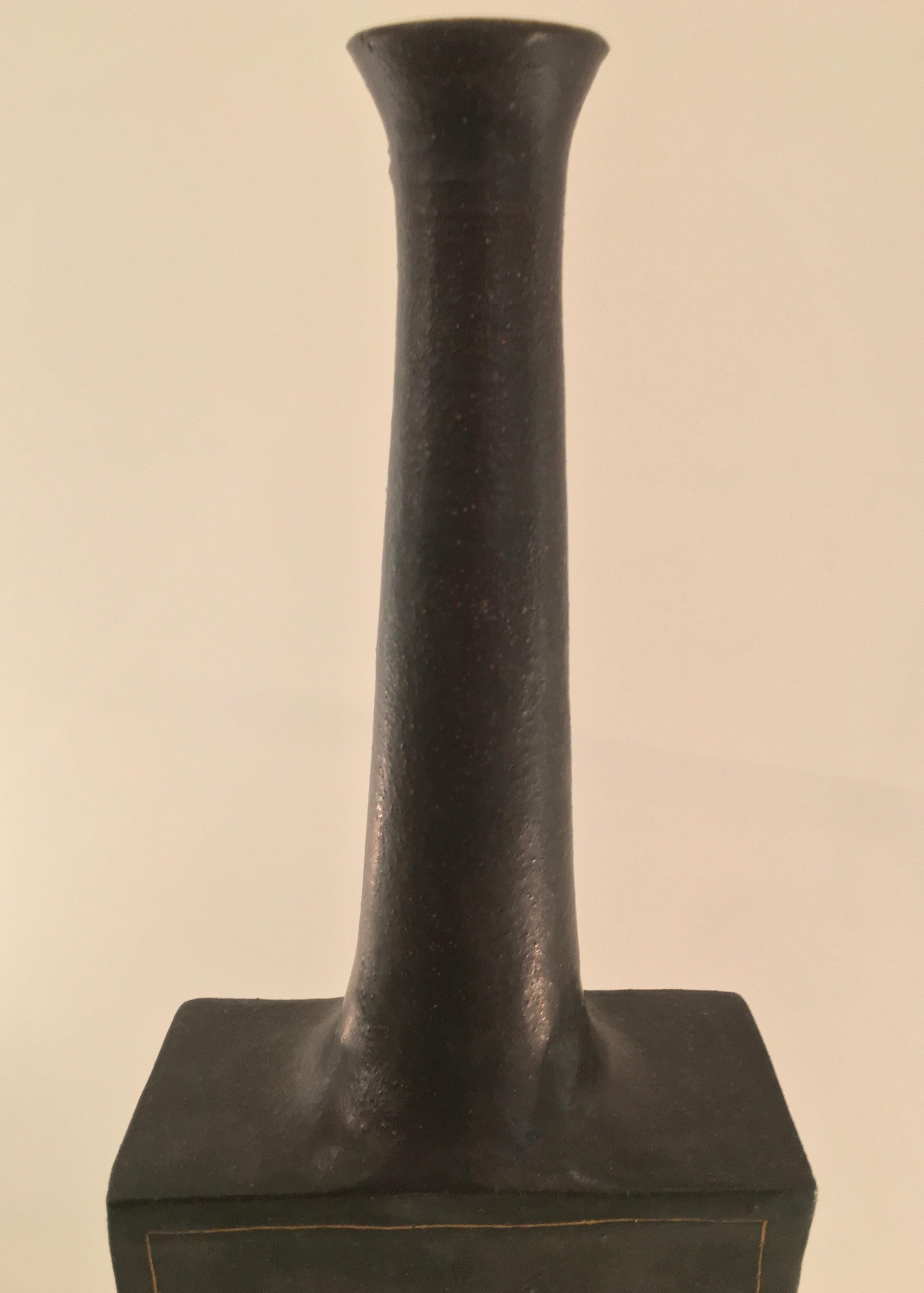 A dark grey glazed ceramic vase with gold detailing by Florentine ceramicist, Bruno Gambone. Designed and produced in the early 1970s, this earthenware rectangular vase with elongated neck is synonymous with Bruno's paired down, minimalist style.