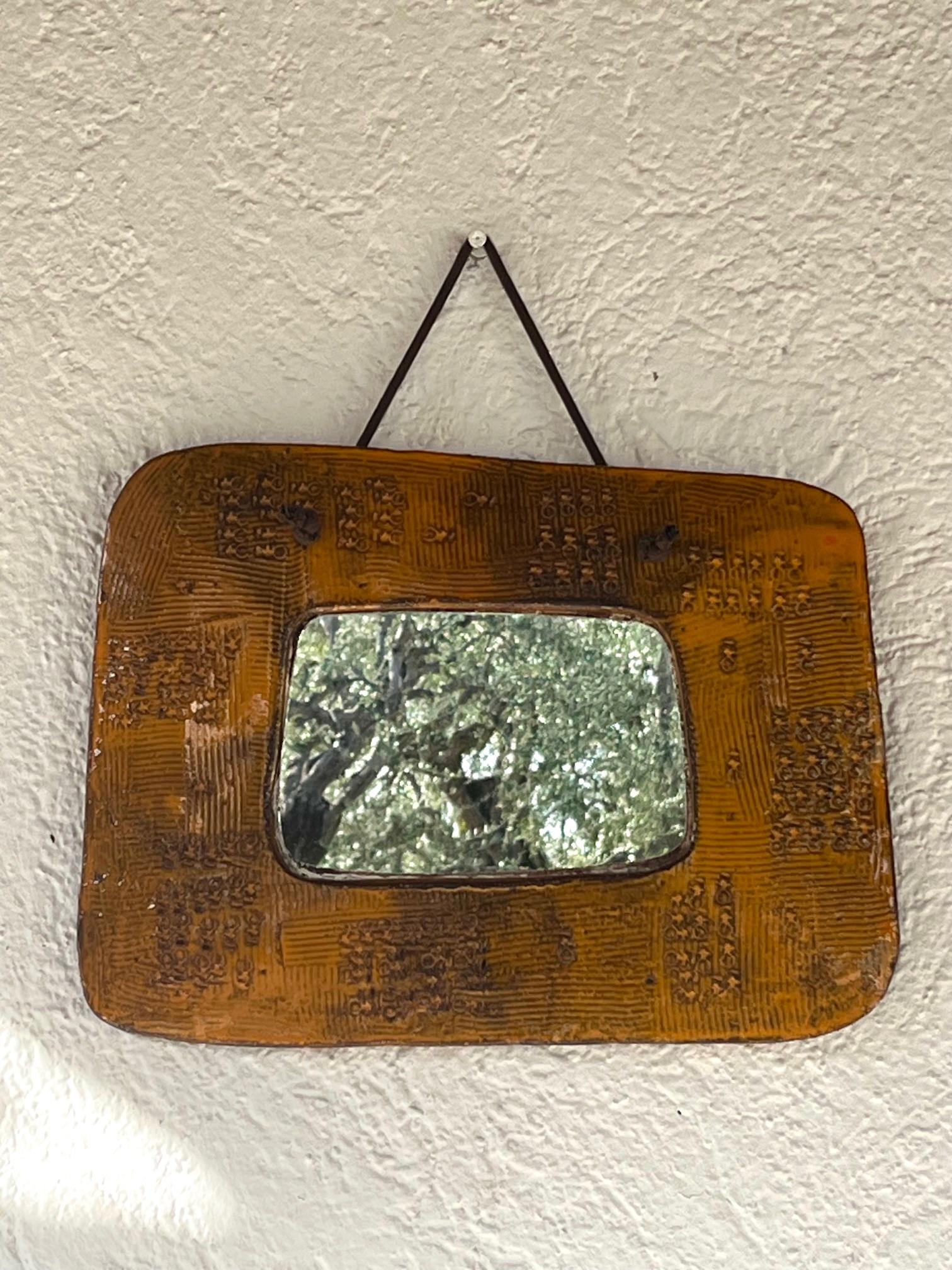 Glazed and stamped free-form ceramic mirror.
Thick curved frame with rounded angles, decorated with scarified and stamped patterns under a shiny orange glaze; 
Signed 