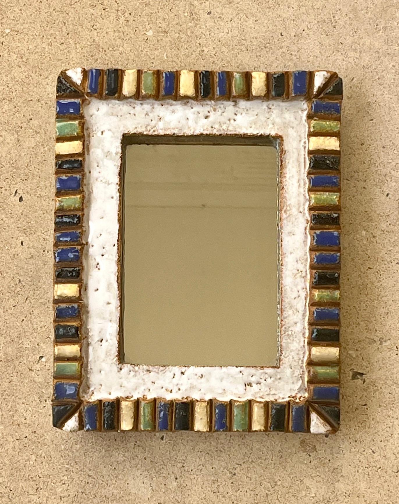 Miroir rectangulaire par les Argonautes. 
Céramique émaillée. 
Cadre plat blanc entouré de cabochons gaufrés blancs, noirs, bleus, verts et jaunes . 
signature portée à  le dos 