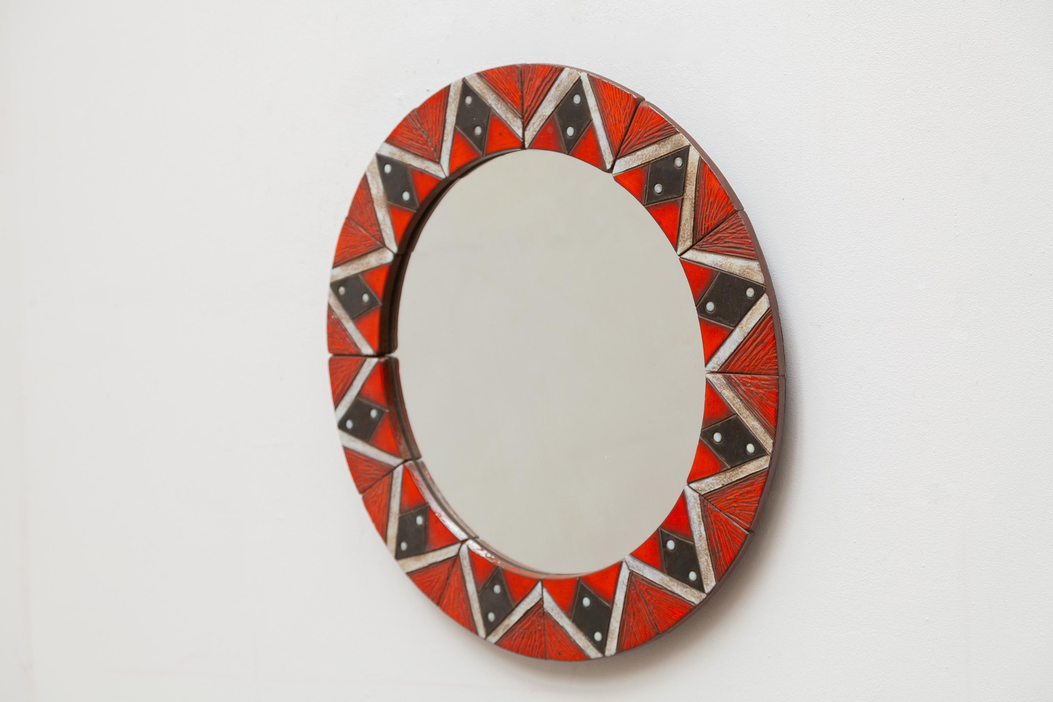 A beautiful example of the work of refined ceramic artist Oswald Tieberghien. The mirror consist of a mosaic geometric inlayed tiles in the colors red, black and white around a wall mounted glass mirror. 

Tieberghien studied at the Sint-Lucas