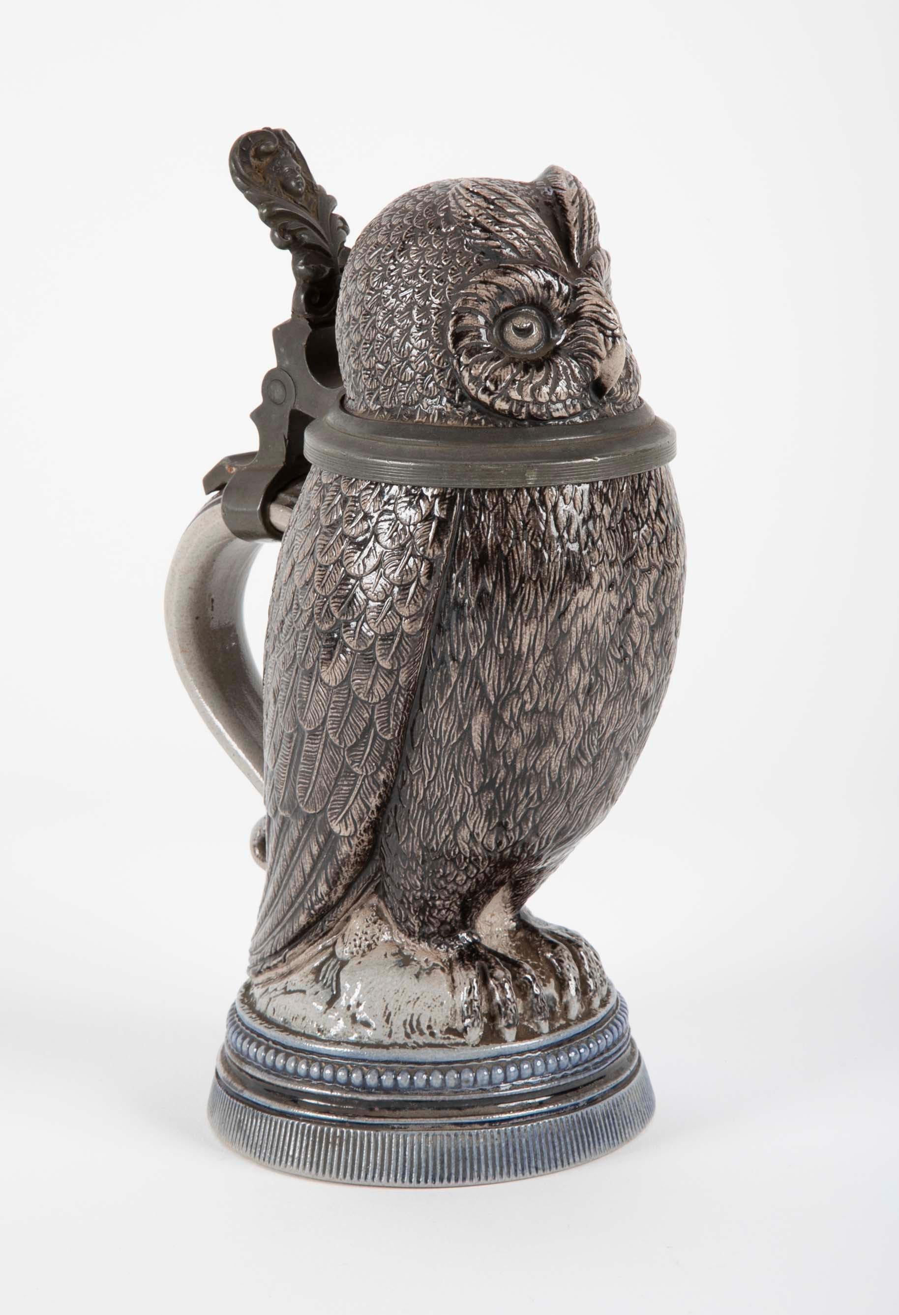 An extremely charming stoneware tankard in the form of an owl. With a two toned gray and blue glaze and handsome pewter mounts. The thumb lift depicting a female face within a heart shaped frame. Likely Mettlach, incised mark on base
