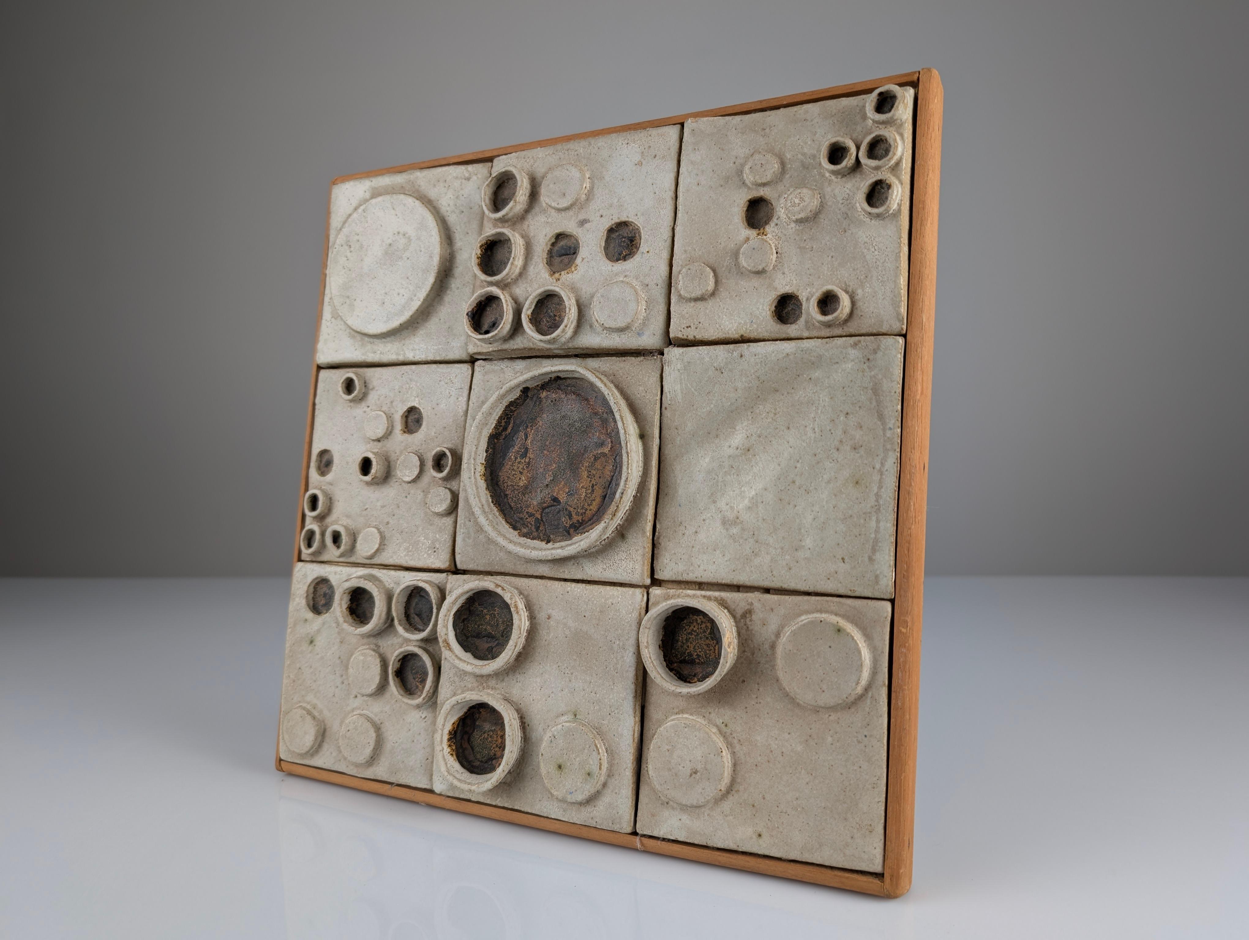 A glazed ceramic plaque composed of nine pieces featuring circular relief designs. This piece showcases an abstract aesthetic that emphasizes intricate ceramic craftsmanship with unique textures and geometric forms. The circular relief composition