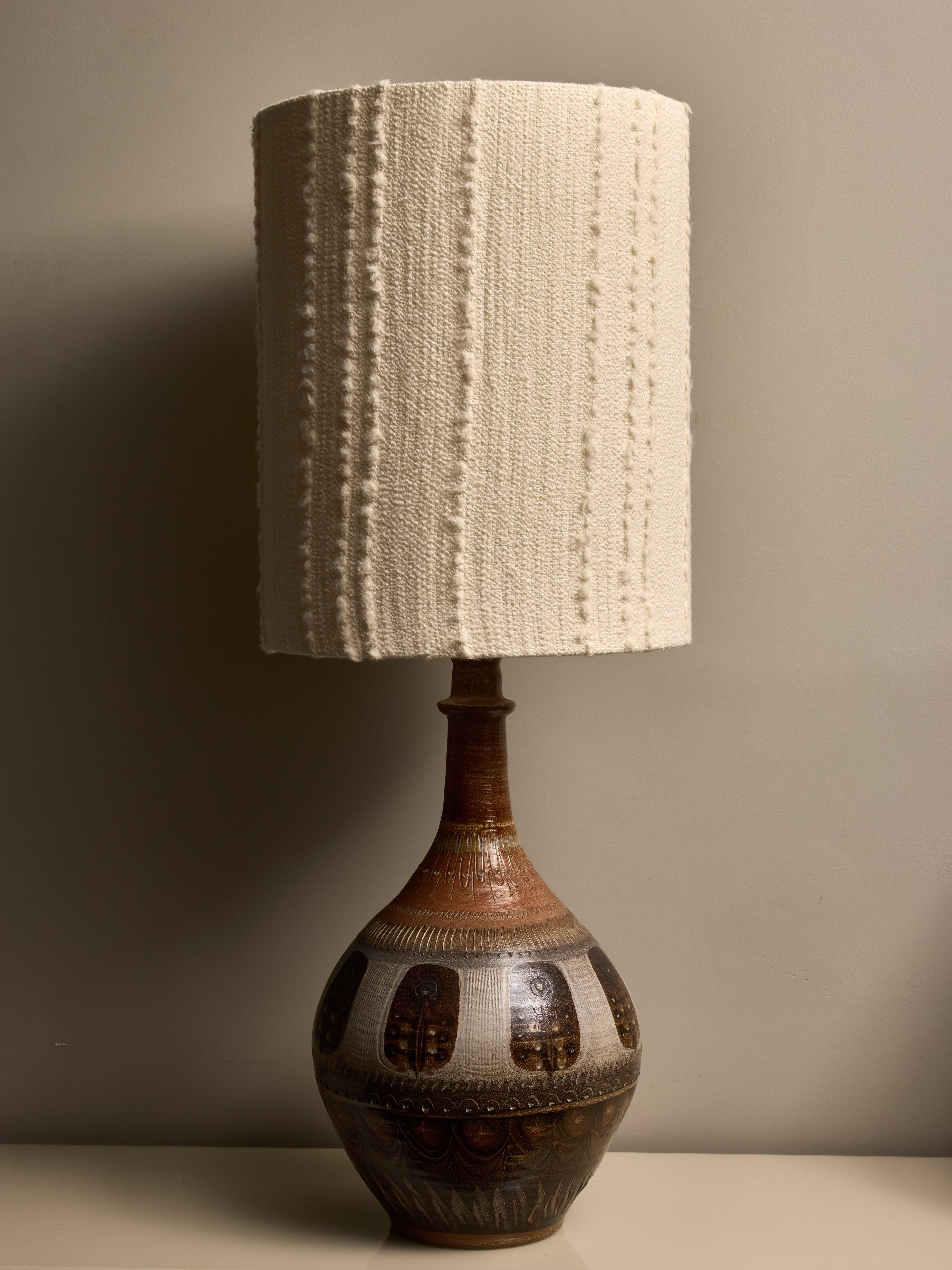 Lampe de table en céramique à la riche glaçure brune et beige, ornée de motifs floraux. Elle est élégamment surmontée d'un abat-jour contemporain et porte la signature d'André l'Helguen sous le socle.

Dimensions avec l'abat-jour : ø40 H105cm

André
