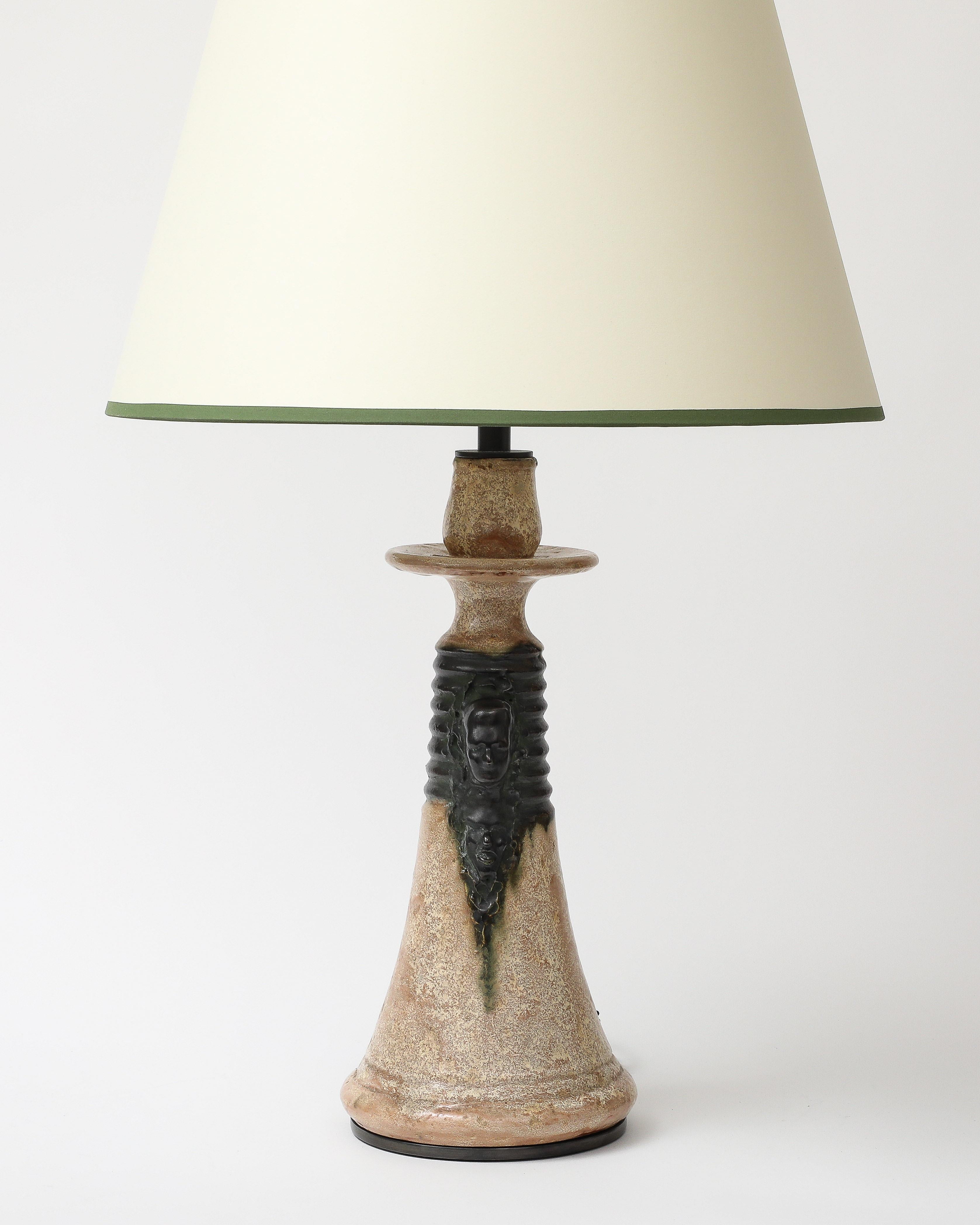 Lampe de table en céramique avec glaçure beige et vert chasseur. Un buste est sculpté dans le col de la lampe, en face de la petite poignée. On dirait qu'il a été fabriqué pour ressembler à un chandelier. 