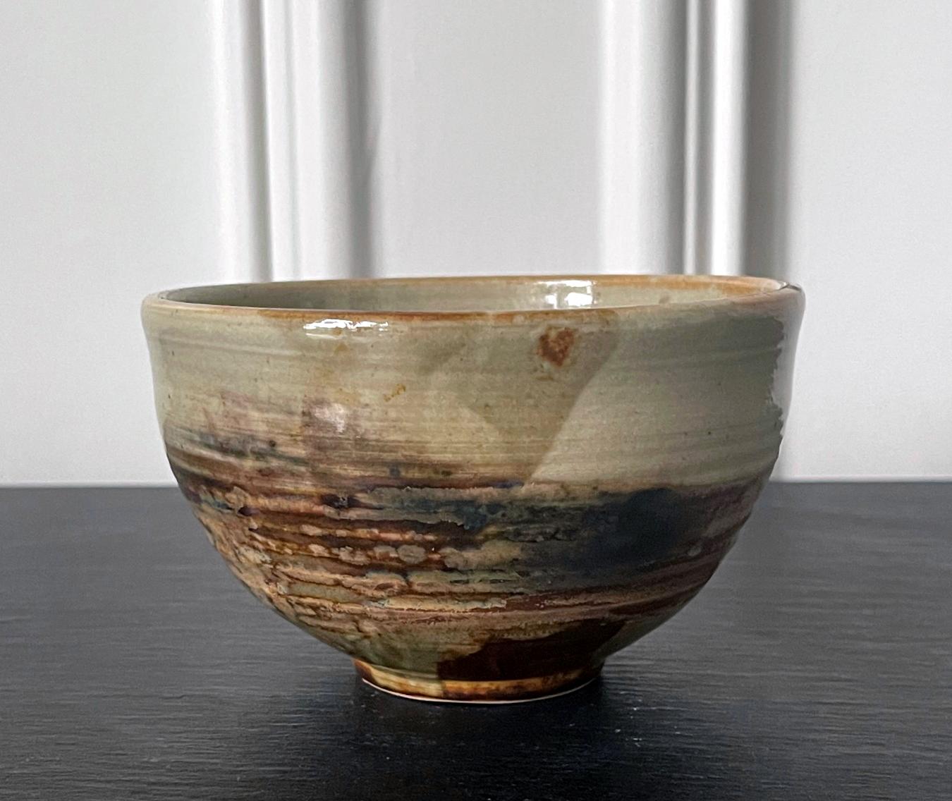 A small elegant glazed ceramic tea bowl (chawan) by Japanese American artist Toshiko Takaezu (American, 1922 - 2011). The well-balanced form is hand built and shows slight irregularity, further accentuated with wheel grooves circumventing the