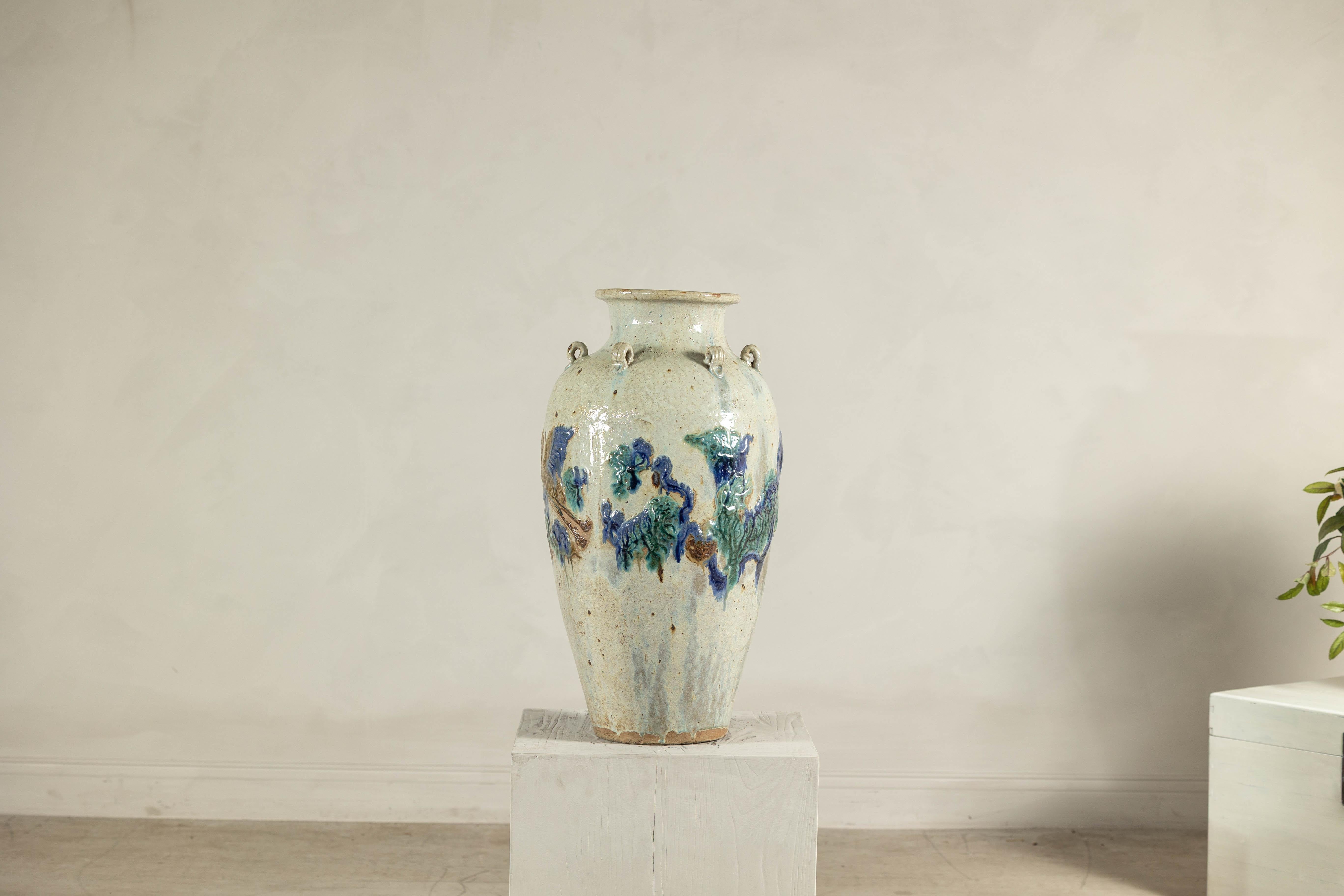 Esta gran tinaja de cerámica vietnamita, probablemente de finales del siglo XIX o principios del XX, presenta decoración aplicada a mano bajo un vidriado feldespático de ceniza. La forma ovoide bulbosa es típica de las tinajas Martaban producidas en