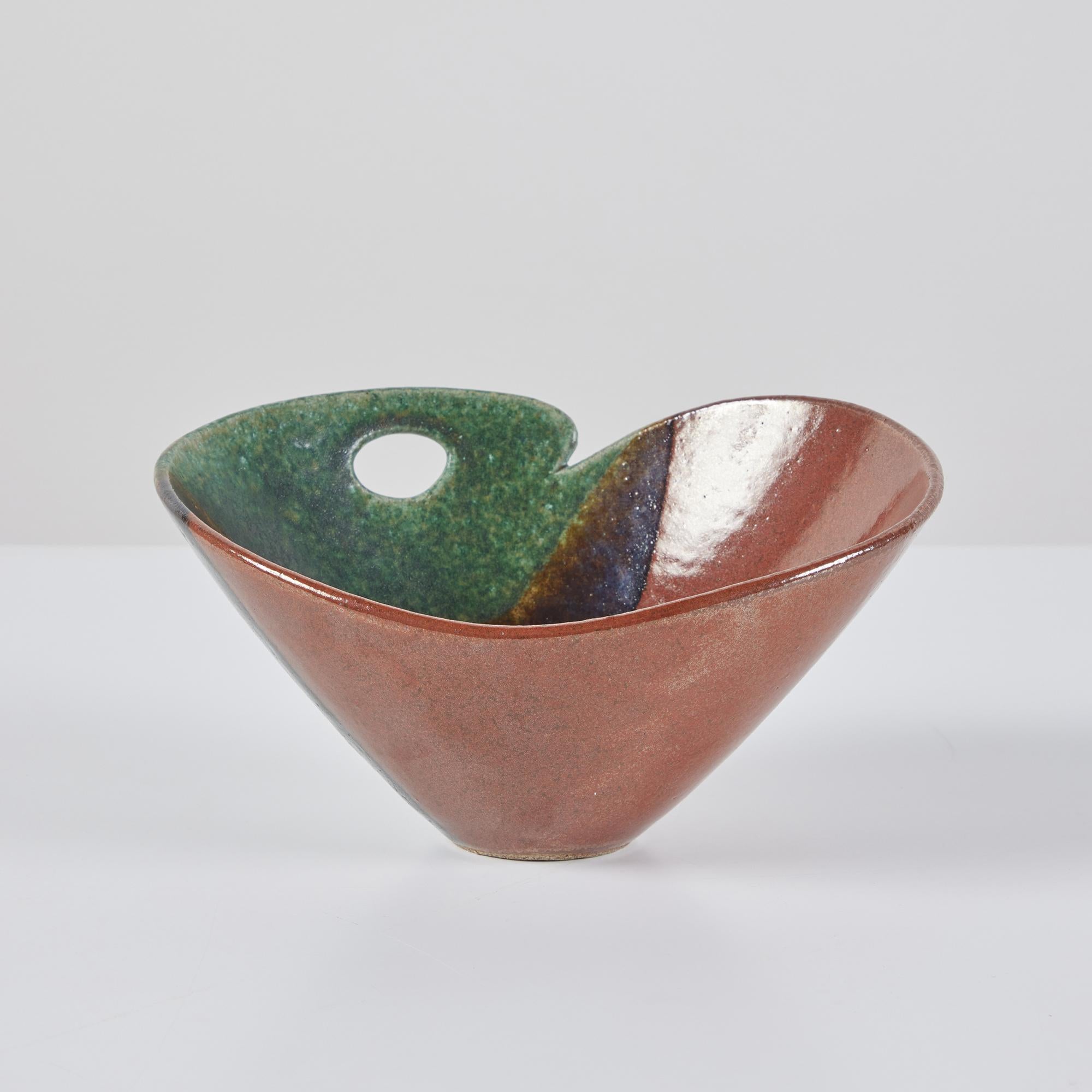 Ceramic bowl in three varying earth tone glazes that range from green to deep brown. The bowl features two higher rounded sides with a divot and an oval cutout on one of the sides.  Signed on the underside. 

Dimensions
8.25