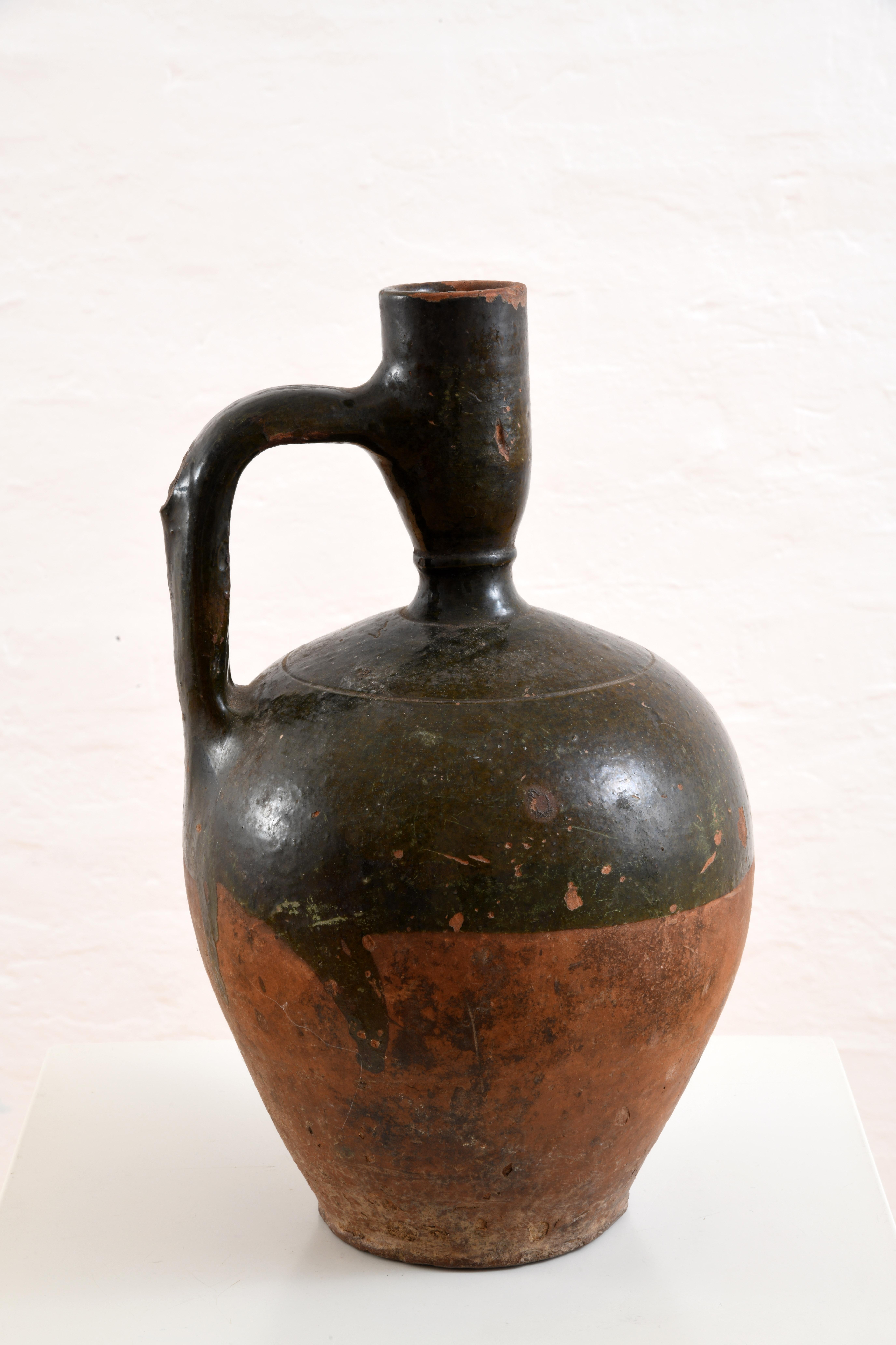Brocca in terracotta smaltata, Francia meridionale, inizio XX secolo. Forma ovoidale con un collo lungo e stretto e un manico, utilizzato per servire acqua o vino. Parzialmente smaltato sulla parte superiore, intorno al collo e al manico, il fondo è