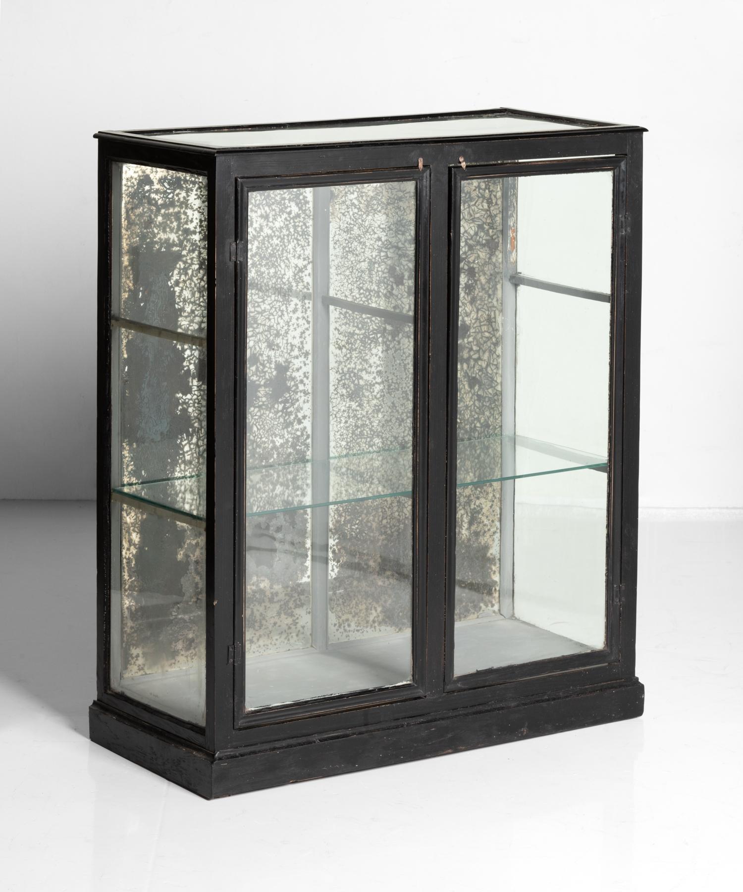 Glazed mirror back display cabinet, England, circa 1900.

Wonderfully sized ebonised form with beautifully patinated mirror back and brackets to hold two-glass shelves.