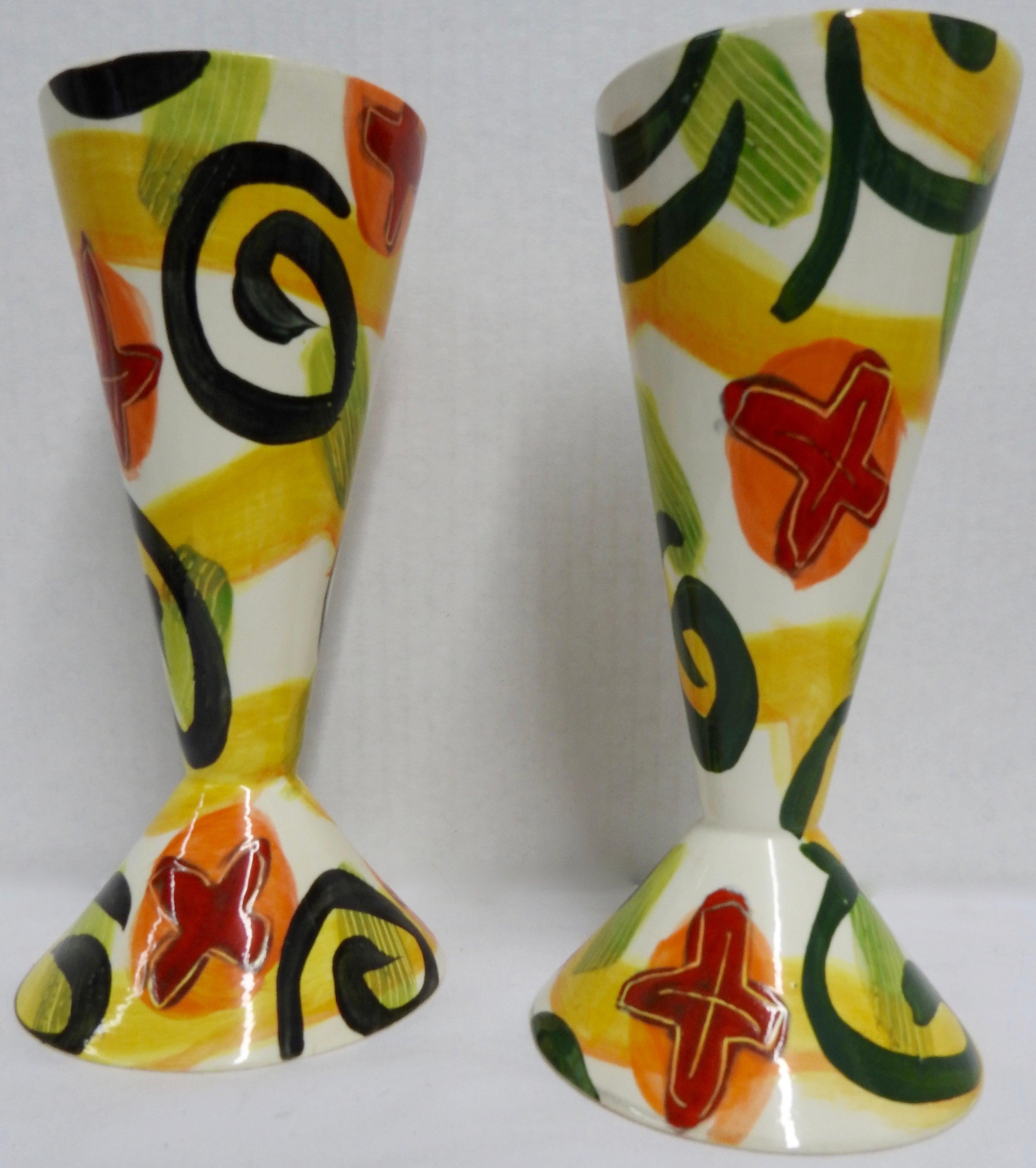 Bold shades of red, orange, yellow and green on white compliment this pair of whimsical goblets by ceramic artist Marilee Hall. The inside is glazed in shiny black. Both goblets are signed on the bottom.