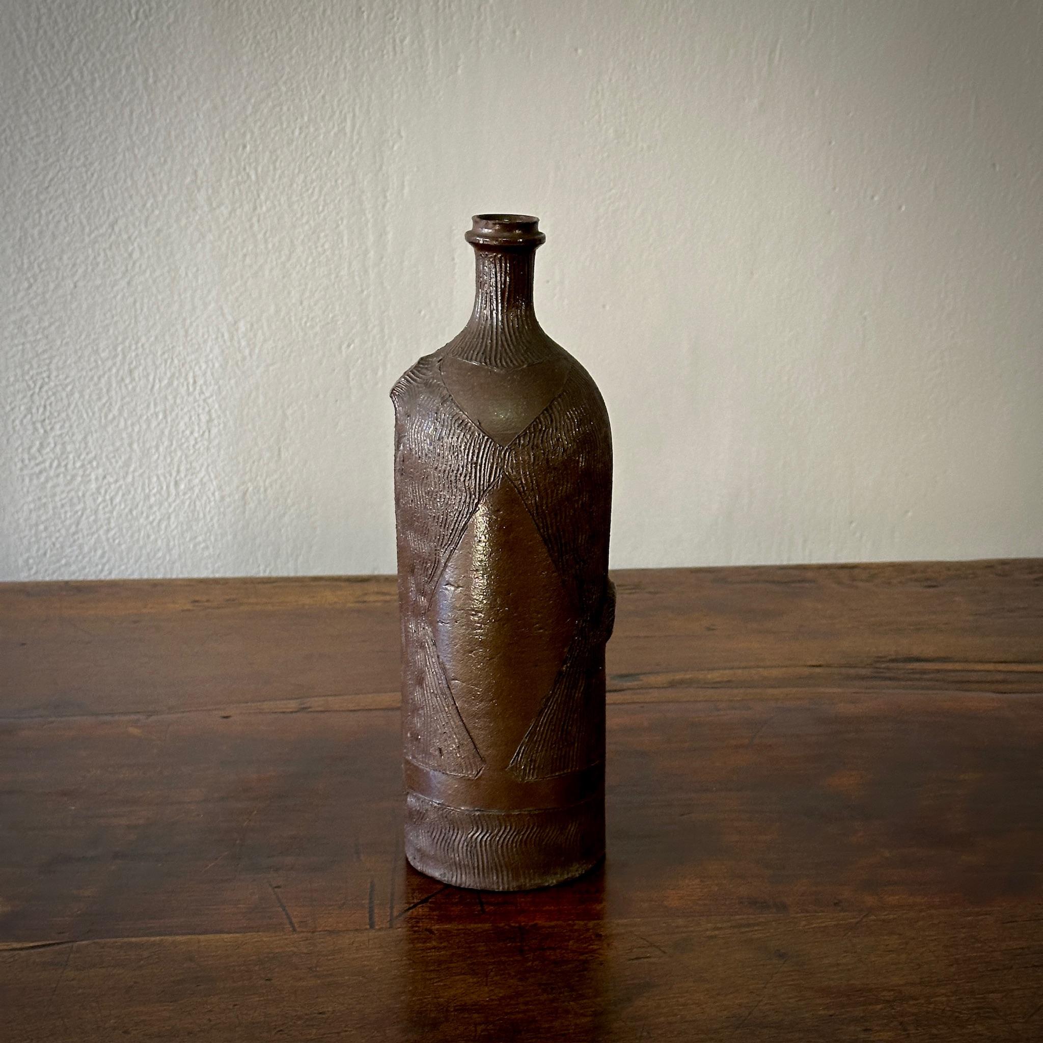 Questa bottiglia di Studio Pottery belga della metà del secolo scorso è splendidamente realizzata con una finitura marrone smaltata e intricate texture intagliate. Il suo design è rustico e raffinato allo stesso tempo, il che lo rende un pezzo