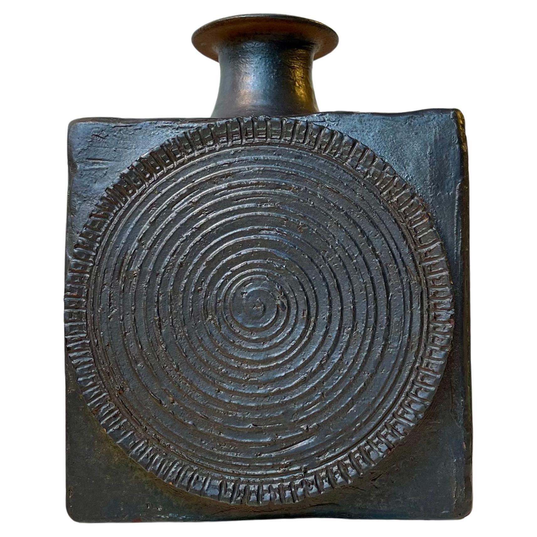 Special Scandinavian vase executed in glazed stoneware. It is square and features a spiraling shield ornament to its front. It has no markings but is Scandinavian studio made and it sure bears close resemblance to designs by Finn Lynggaard and