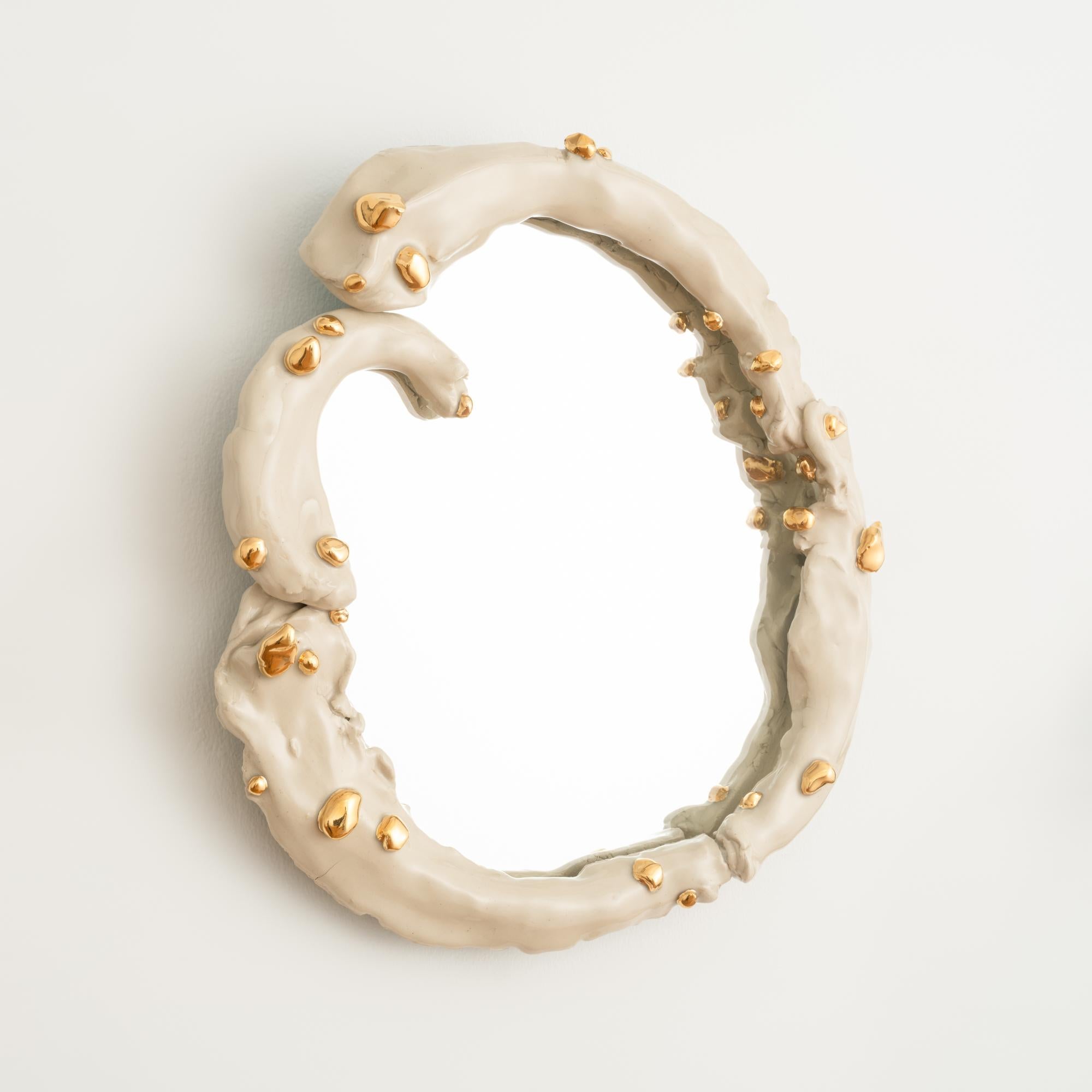 This one-of-a-kind circular wall mirror features a hand-built stoneware frame finished in a glossy cream-colored glaze and embellished with blob-like applications of 22k gold luster. 

Both functional and visually striking, this ornate and