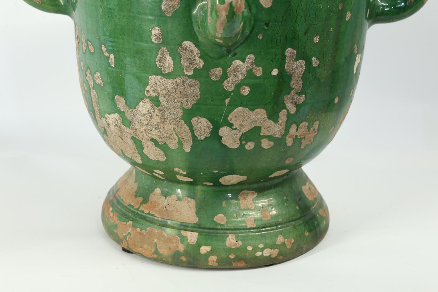 This is a lovely green glazed planter from Anduze, France with four handles and a footed base. The beautiful green glaze has worn in some places leaving a beautiful patina. Please note that the total diameter including the handles is 21 inches while