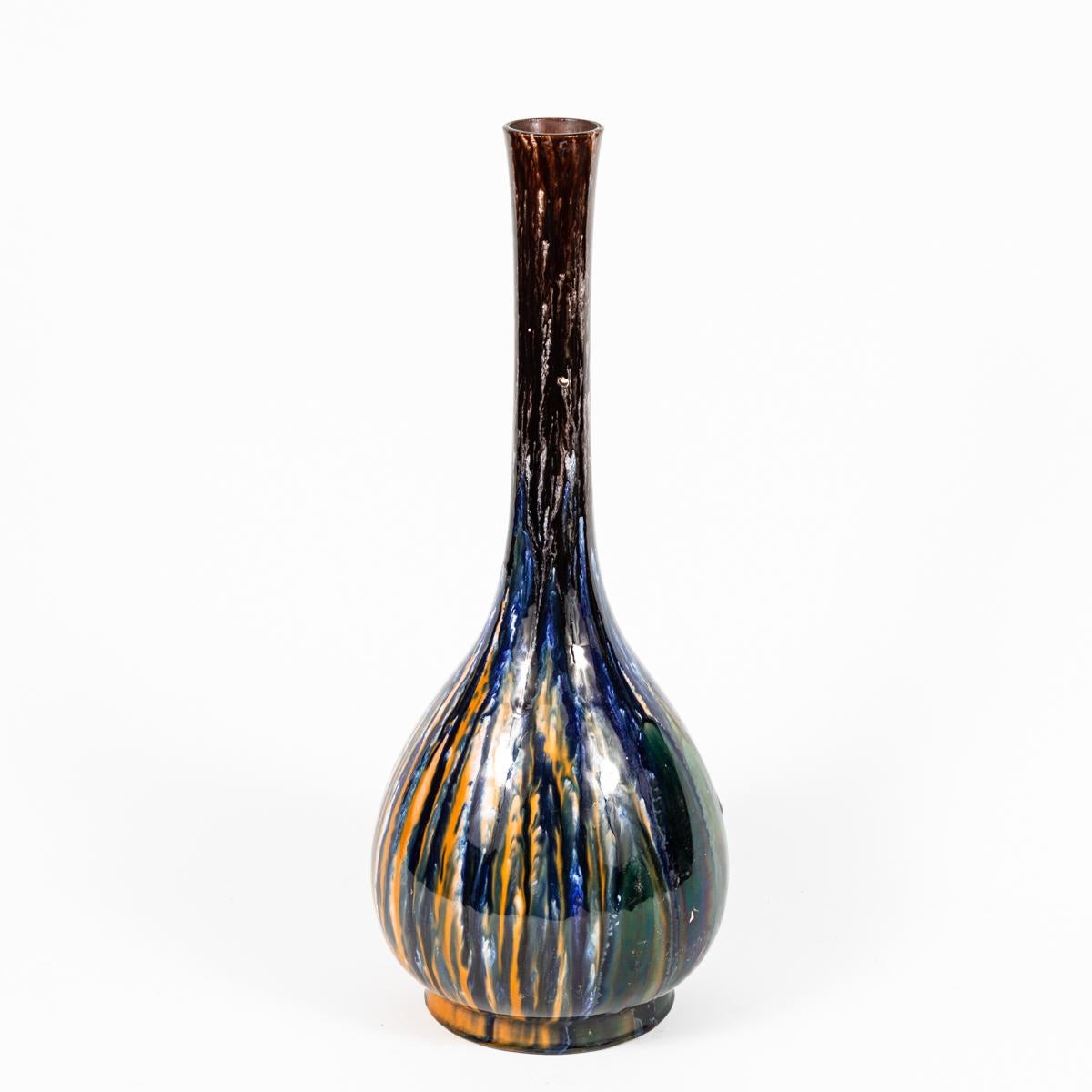 Victorian studio pottery vase with abstract drip pattern. A multicolored glazed ceramic drip-ware vase with a blend of colors ranging from orange and brown to indigo and white. The colors are gesturally expressed in vertical strokes that trickle