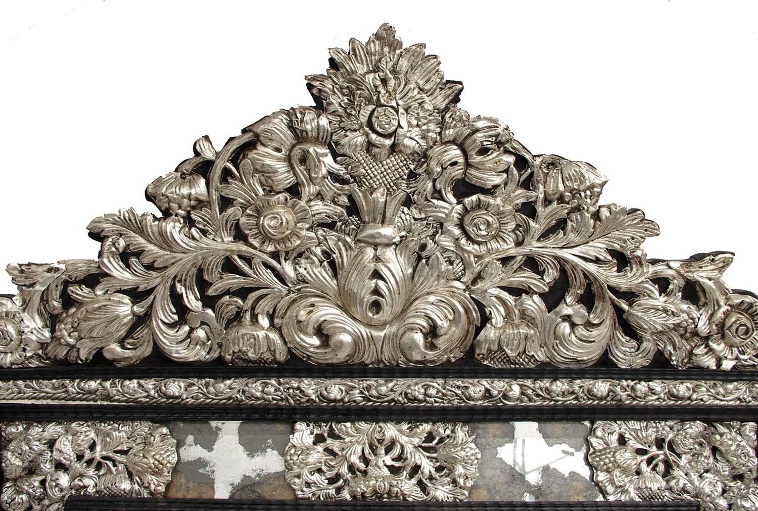 Glazing beads Regence style mirror in embossed silvered brass and blackened wood. Rectangular shape, with edges in mercury mirror decorated with spandrels and central motifs of foliage scrolls, flowers and stylized fruits. Several frames in silvered