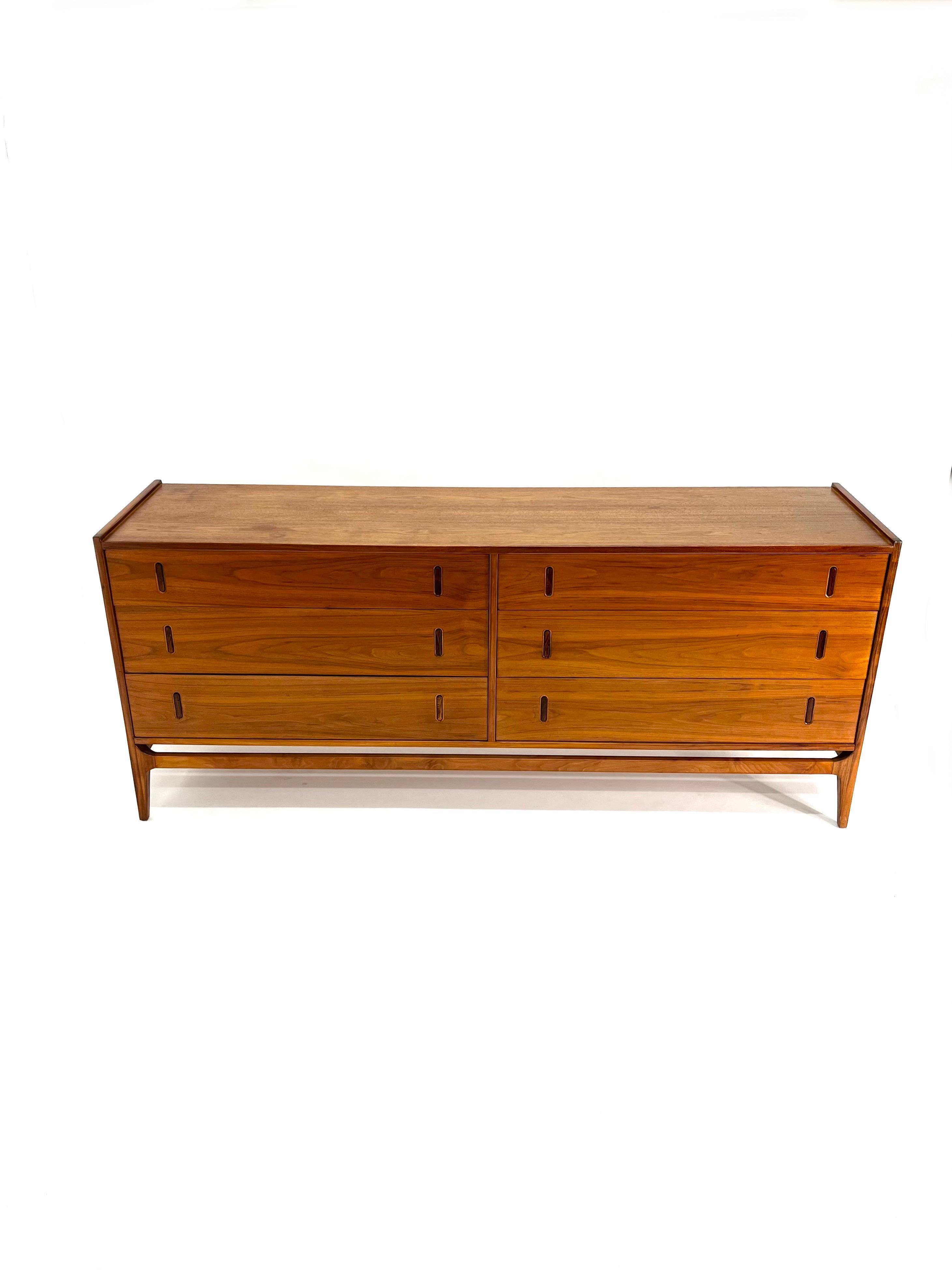 This incredible 6 drawer dresser was designed by Richard Thompson for Glenn of California circa 1950s. It has a sleek walnut wood case with integrated legs and retractable inlaid rosewood pulls, which pop out when the top is pushed. We are huge fans