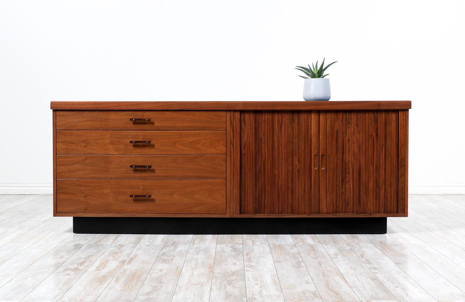 Mid Century Modern Credenza designed by Glenn of California for Glenn of California in the United States c. 1950’s. This beautiful storage piece is comprised of walnut wood. The right side features two tambour doors with recessed pulls that reveal a