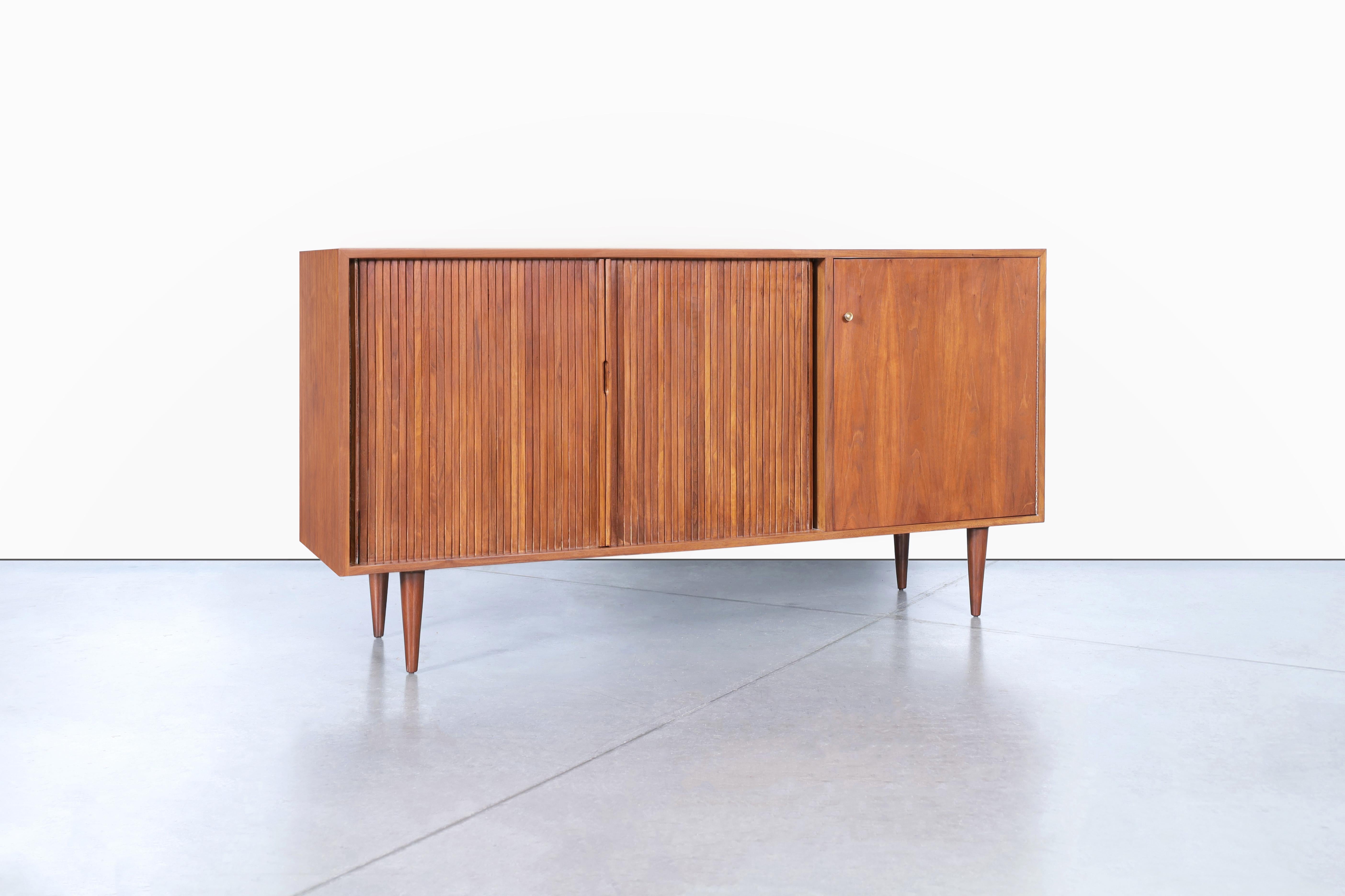 Introducing a stunning mid-century modern tambour door credenza, meticulously designed by Milo Baughman and expertly crafted by Glenn of California in the 1950s. This exquisite piece features a sleek walnut frame, supported by tapered legs, and is