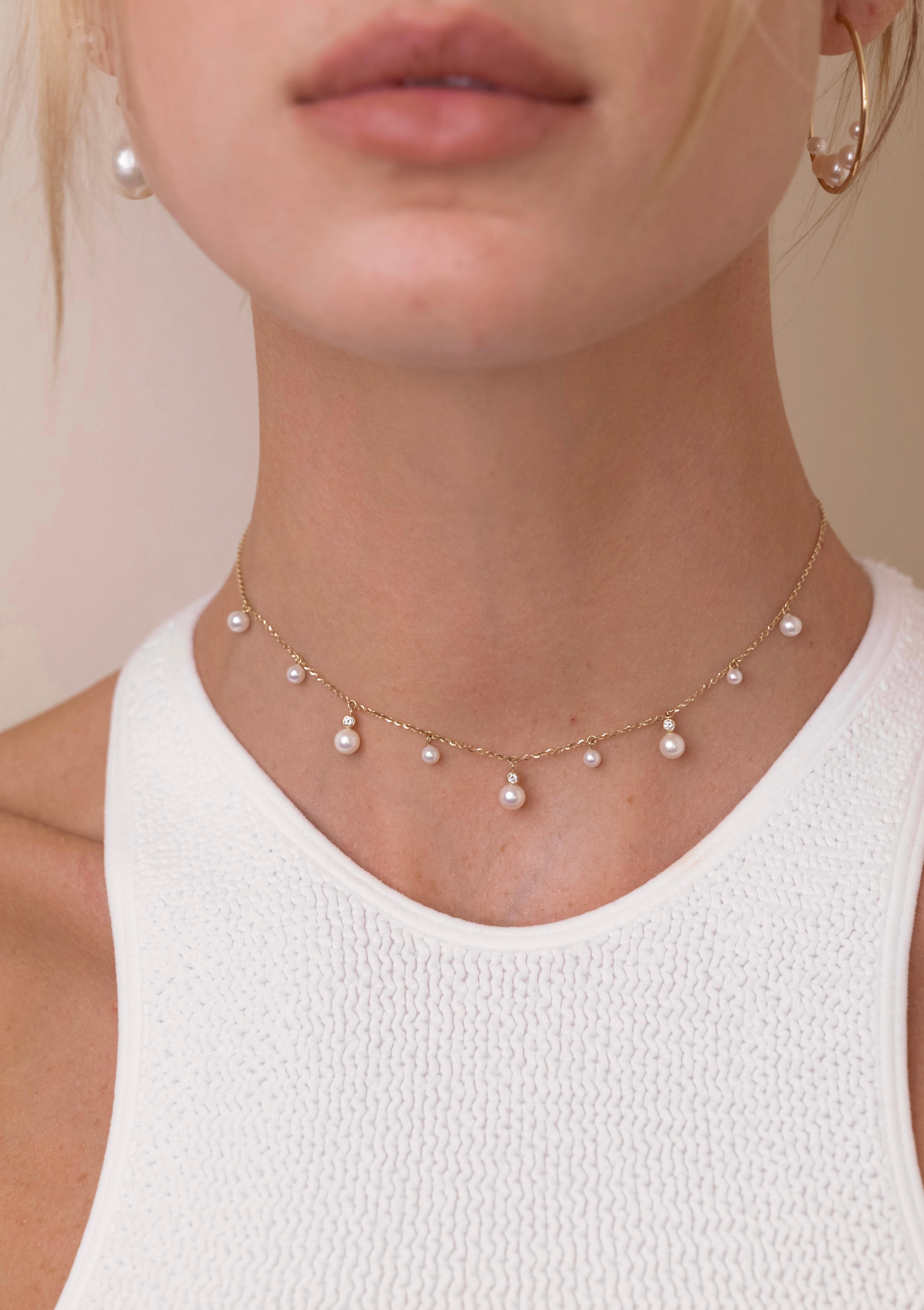Una serie di perle penzolanti di varie dimensioni accentuate da diamanti scintillanti che pendono da una delicata catenina stretta intorno al collo. Una rivisitazione moderna del classico girocollo di perle, che aggiunge un tocco di allegria a