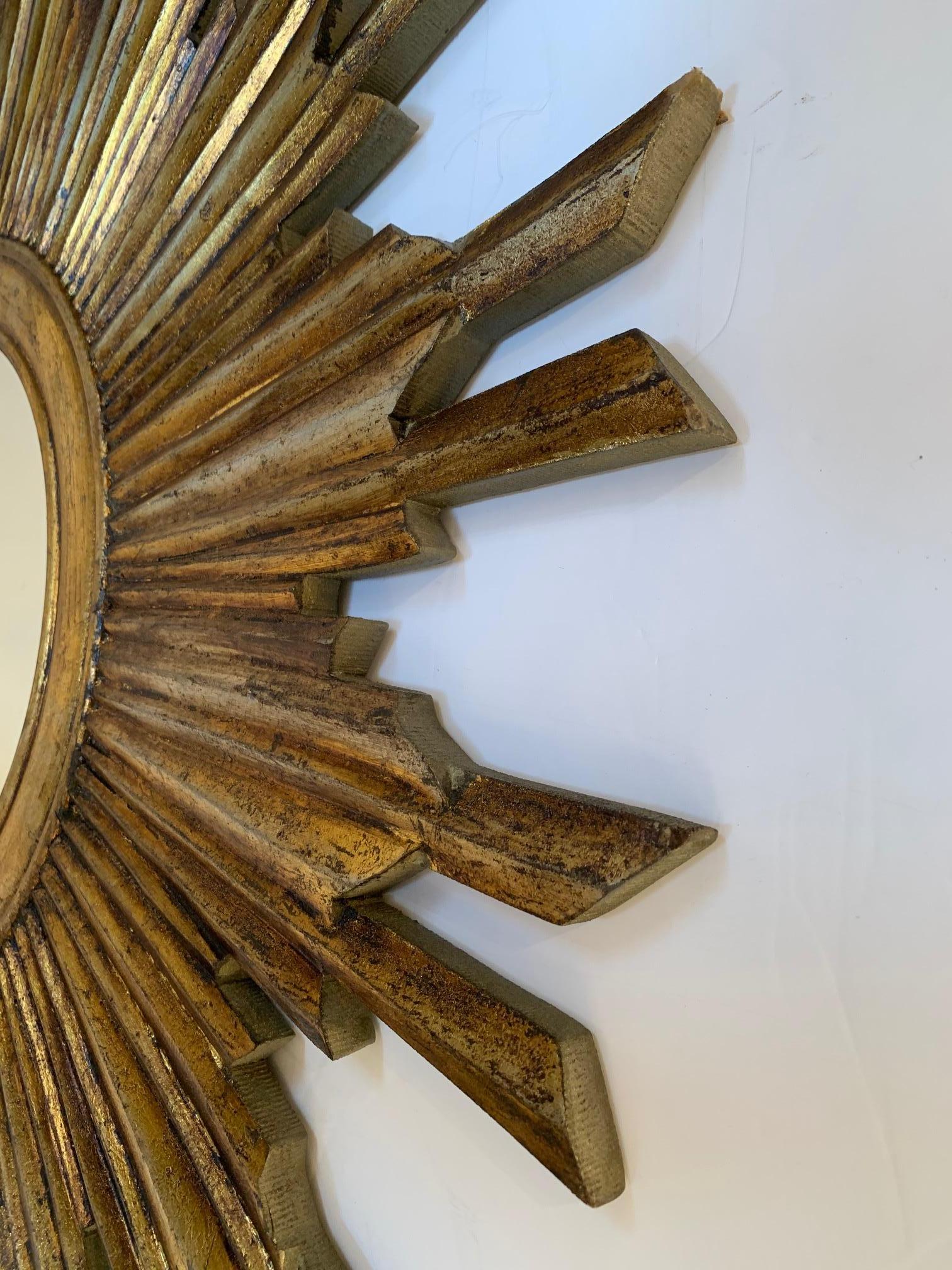 Classic vintage giltwood sunburst mirror with varying lengths of rays around a circular mirror.