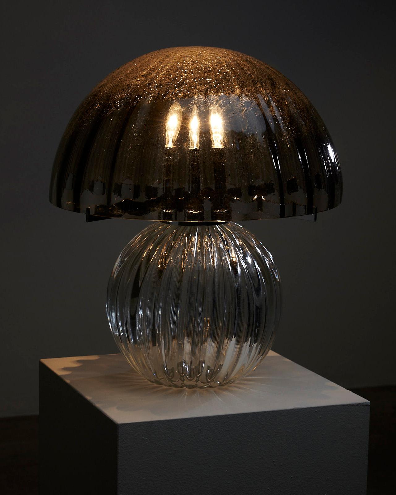 Introducing the Glimmering Glass Mushroom Table Lamp, a stunning piece that combines the beauty of darker blackish bubble glass with transparent bubble glass. This lamp showcases a perfect fusion of form and functionality.

The base of the lamp is
