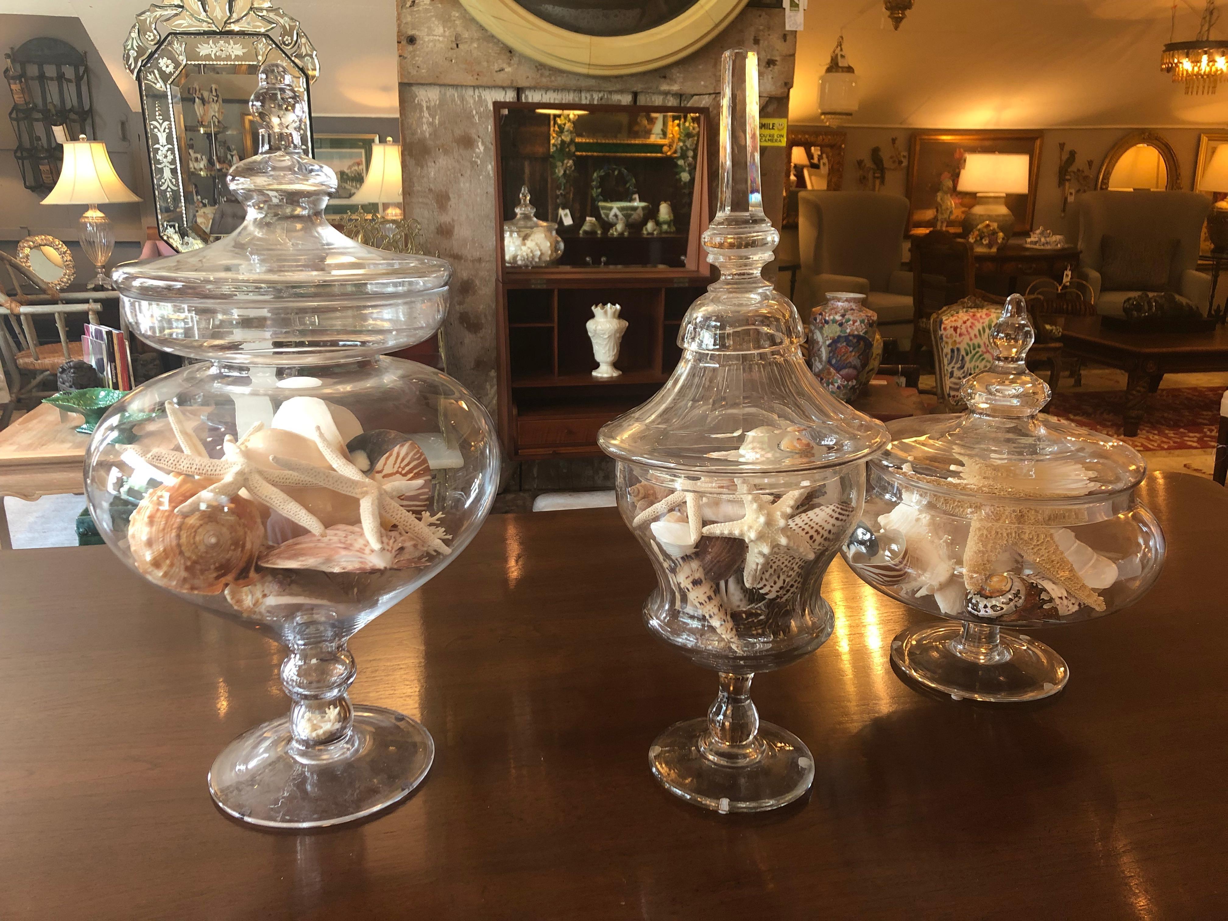 A gorgeous trio of 3 large lidded urns to accessorize dining table, console, center hall or mantel.
They are:
1- 19th century crystal with elongated columnar finial 25 H 10 W 10 D
2- Largest, tallest glass urn 24 H 12 W 12 D
3- Squat large urn