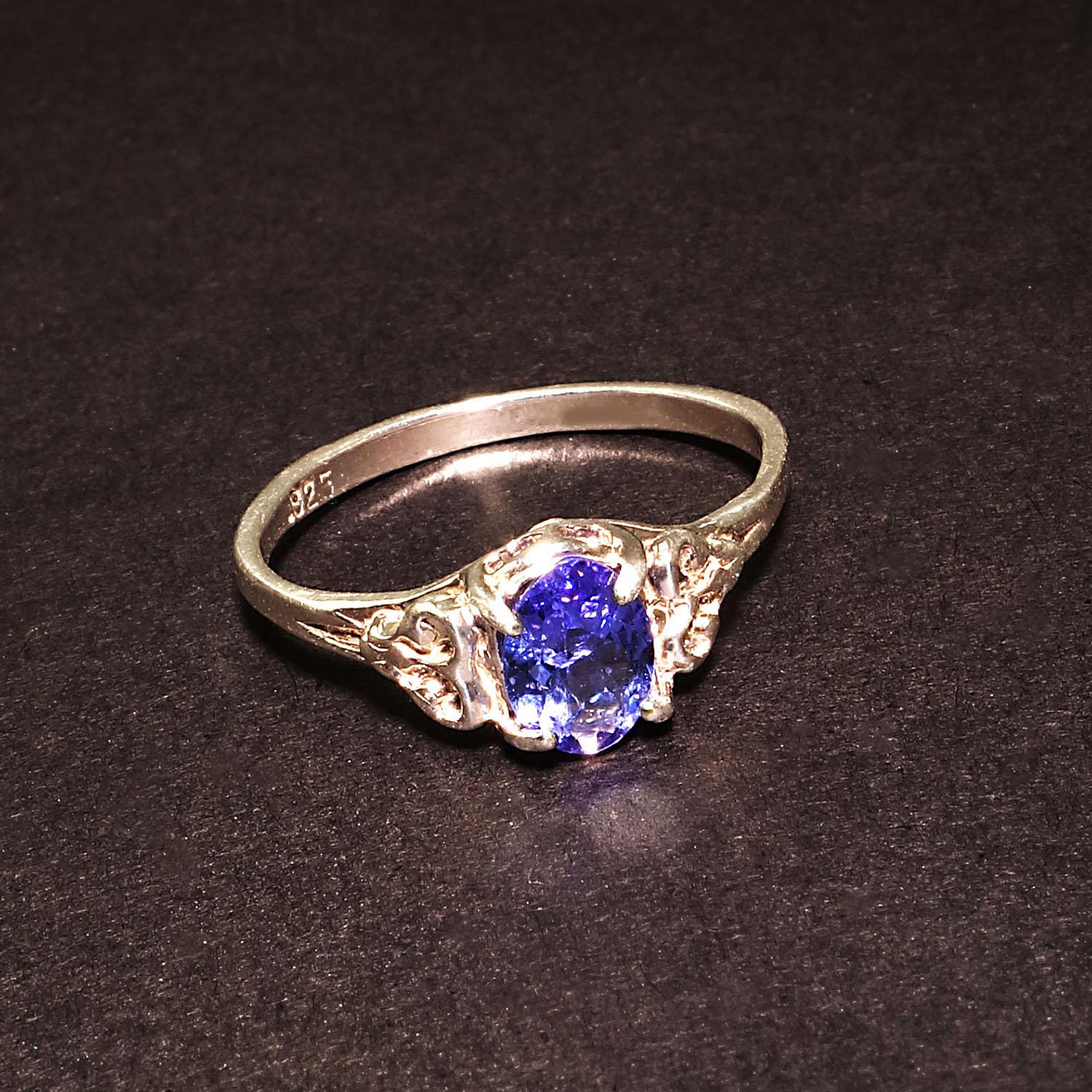 Custom designed ring featuring an oval Tanzanite nestled in a Sterling Silver setting of free form scrolly hearts and detail work descending to a single Sterling Silver band.  The detail in the setting perfectly sets off the sparkling 7x5MM