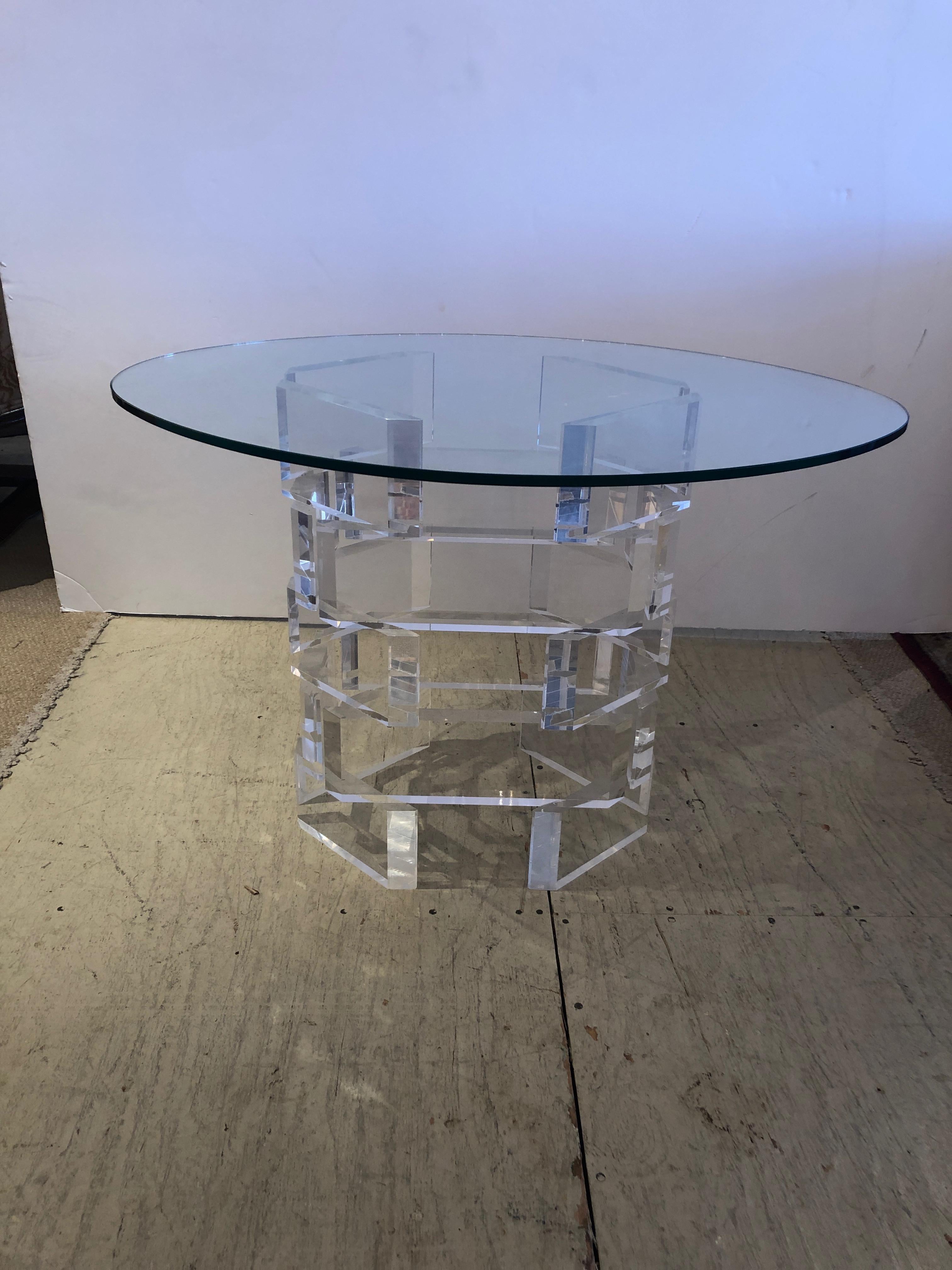 Like a glistening piece of jewelry, a chunky Lucite based side table having stacked pieces of transparent acrylic with a base measuring 17 W, 12 D, 21 H. An oval piece of glass is on top, but size and shape could vary as pedestal could support