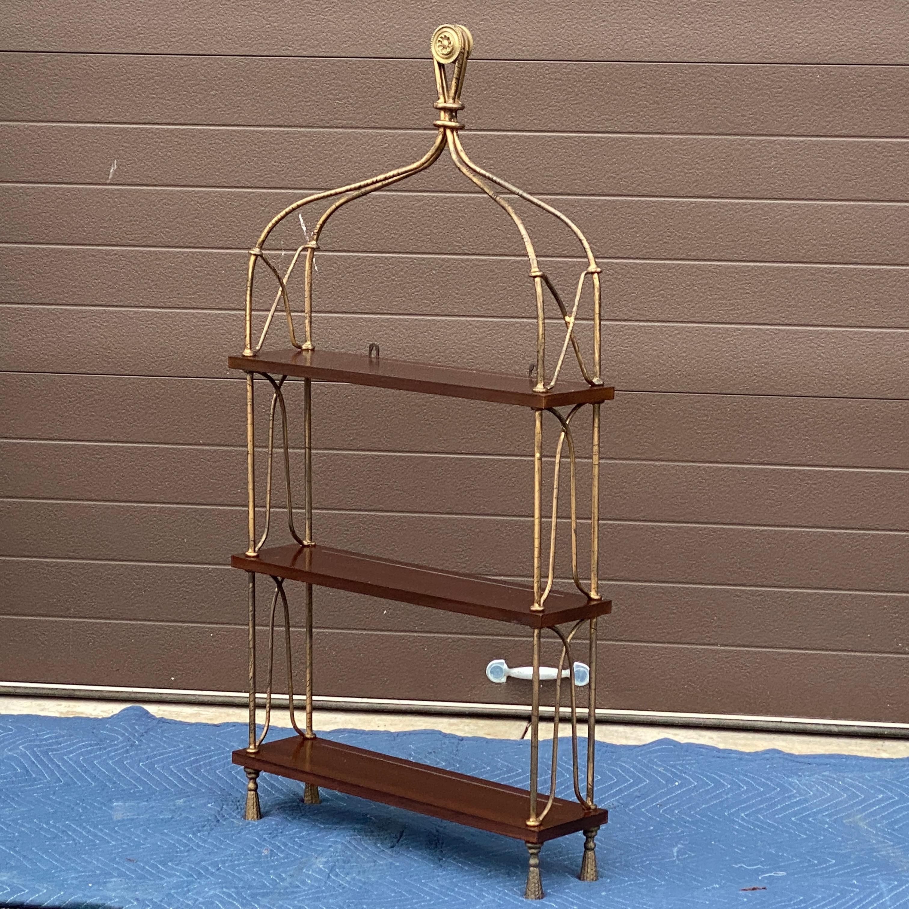 Global Views Wall Mounted Etagere
Antiqued gilt wrought iron frame with tassel feet, knotted framework, and looped brass finial, all supporting three mahogany finished shelfs. 
Lower shelves clearance roughly 11” 
Top shelf variable clearance 8