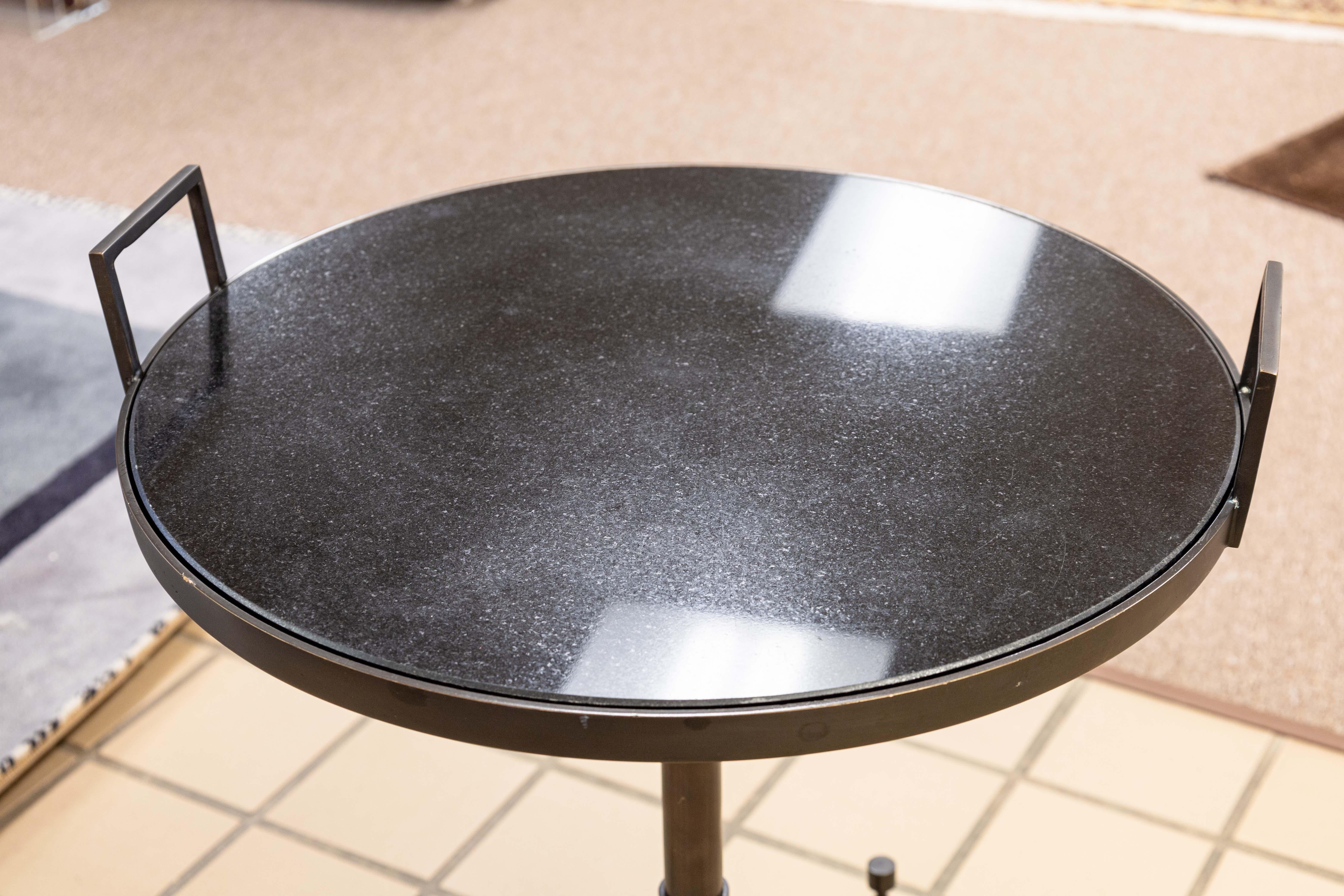 A Global Views side end table with casters. A lovely little side table with a contemporary modern design. This table features a lift top black stone table top. The frame is fully cast in metal, made to resemble a adjustable chair column. The table