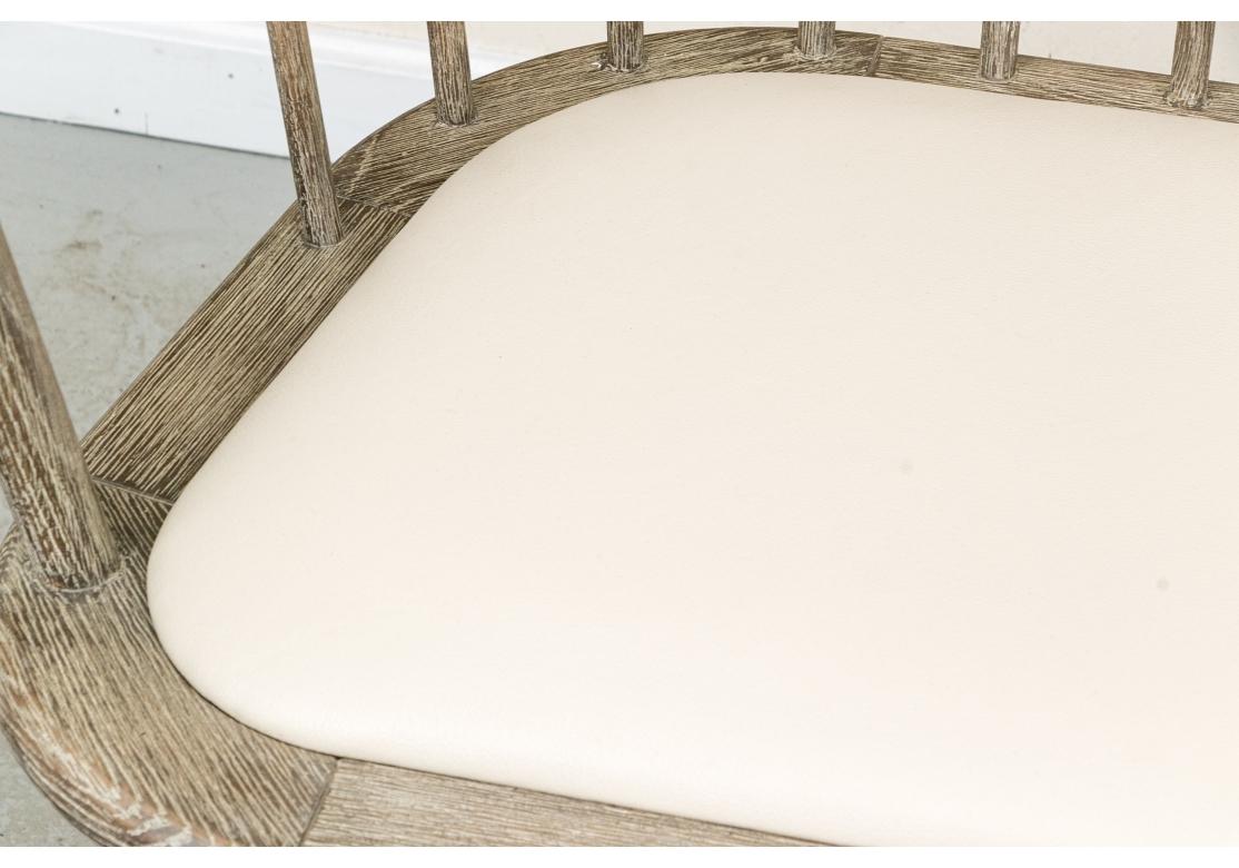 Banc rustique en bois de style Windsor, bien fabriqué, avec un dossier en fuseau et une barre d'assise incurvée. Le banc repose sur dix pieds avec des supports de brancard pour la stabilité structurelle. Le siège est doté d'un coussin en cuir pour