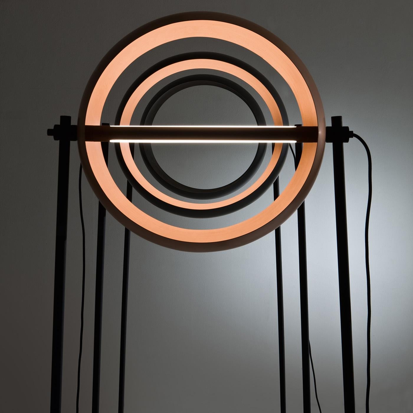 This captivating floor lamp is an exclusive award-winning design by Edoardo Colzani that features a finely sculpted metal base, a distinctive central pivot, and an entirely hand-crafted satin copper rotating lampshade. The warm LED lighting enhances