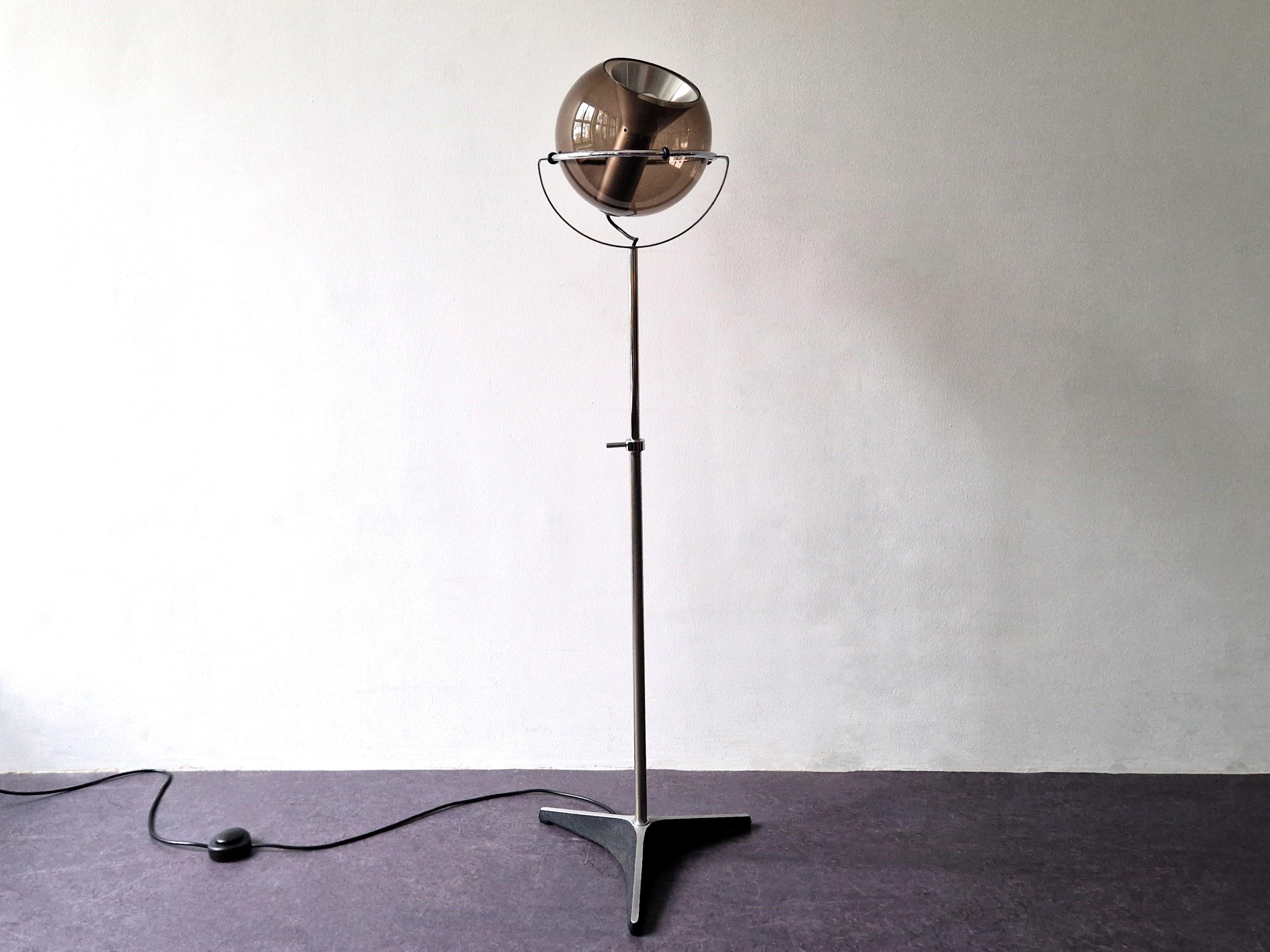 The 'Globe D-2000' floor lamp was designed by Frank Ligtelijn for Raak Amsterdam in the late 1950's. It has a classical smoked glass globe, with an aluminum reflector and lamp holder, standing on a chromed metal adjustable rod and cast iron tripod