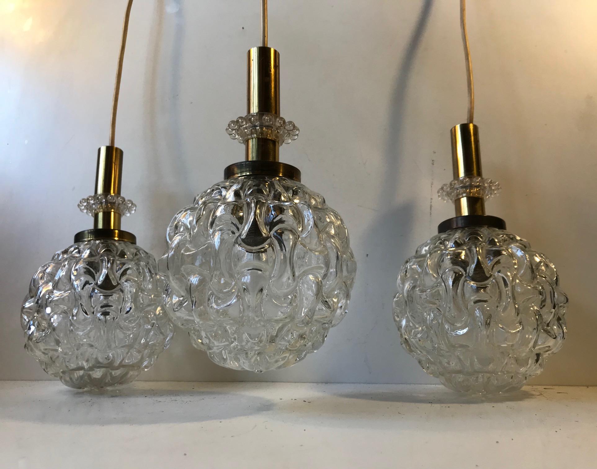 A matching trio of spherical pendant lamps fashioned out of pressed clear glass set in a solid brass top and bejeweled with a clear Lucite manchette. They came out of a Hotel in Leipzig, Germany.
