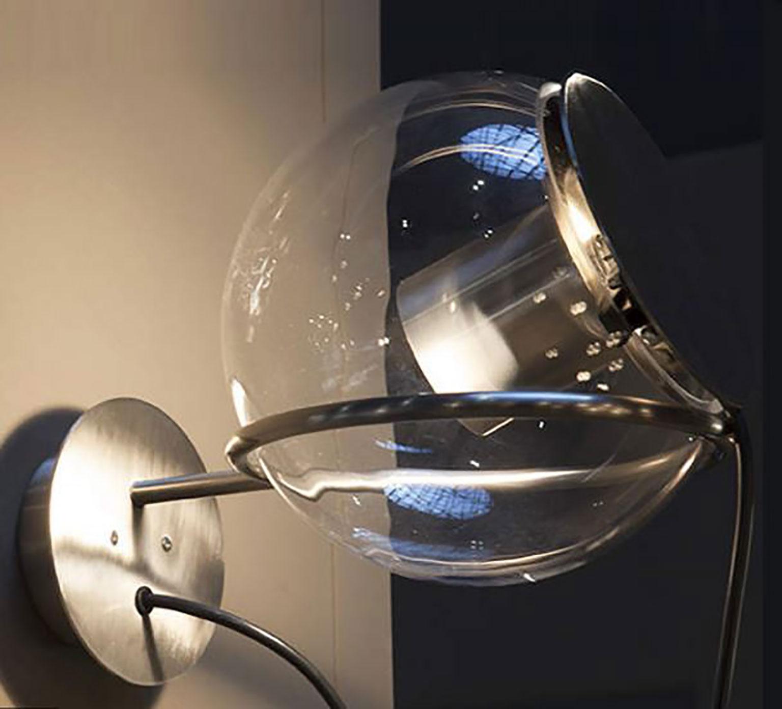 Globuswandleuchte von Joe Colombo für Oluce. Die Gesamtform der Leuchte ähnelt der Form eines Globus, der auf einem Ring sitzt und beliebig positioniert werden kann. Die transparente Kugel besteht aus geblasenem Glas, das auf einem runden Metallring