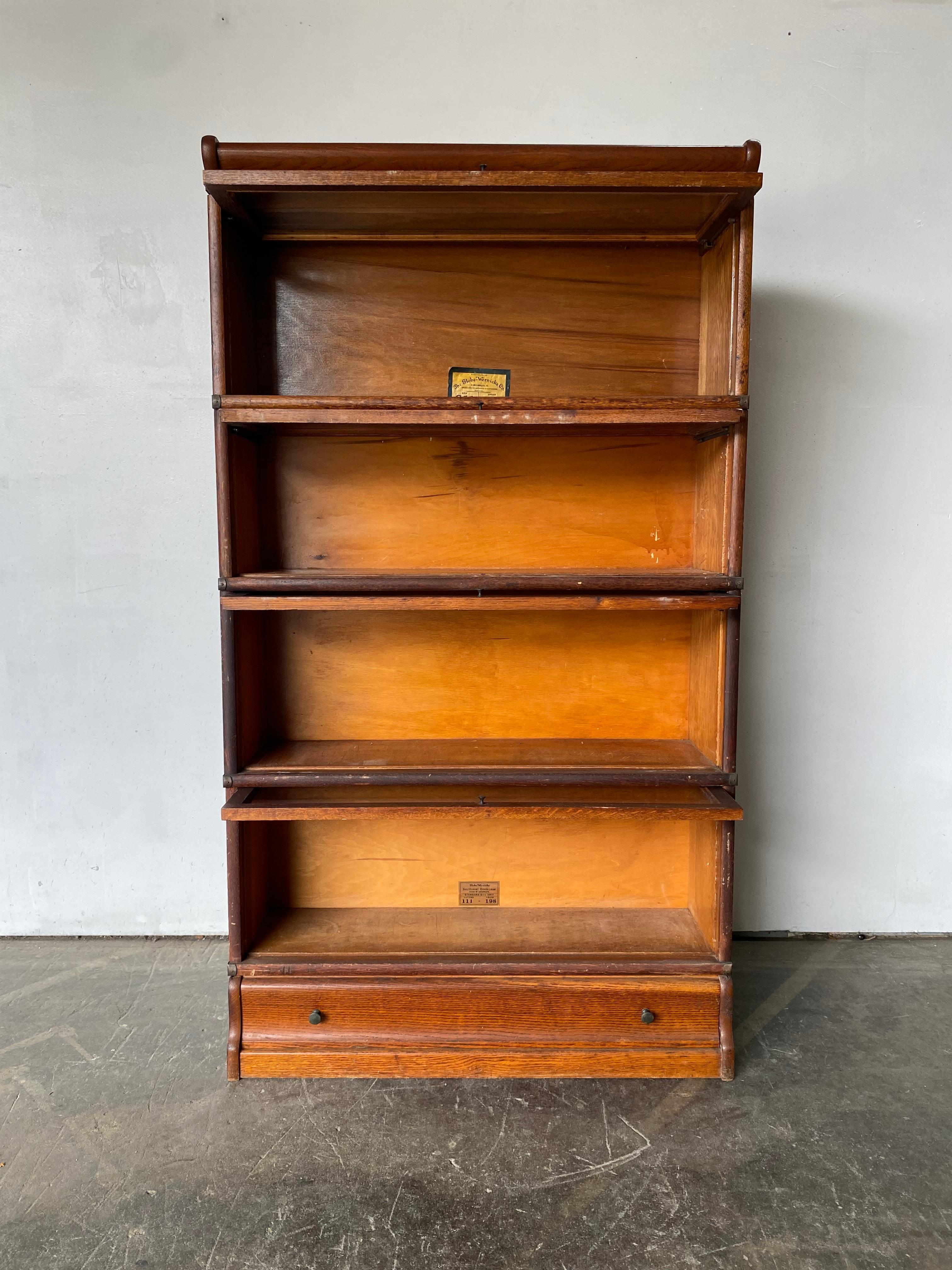 Globe Wernicke barrister bookcase with four stacking shelves and bottom drawer. Manufactured in Cincinnati, Ohio, this piece is made of quarter sawn oak with original metal hardware and glass doors. Original labels intact, grade 198, varying labels