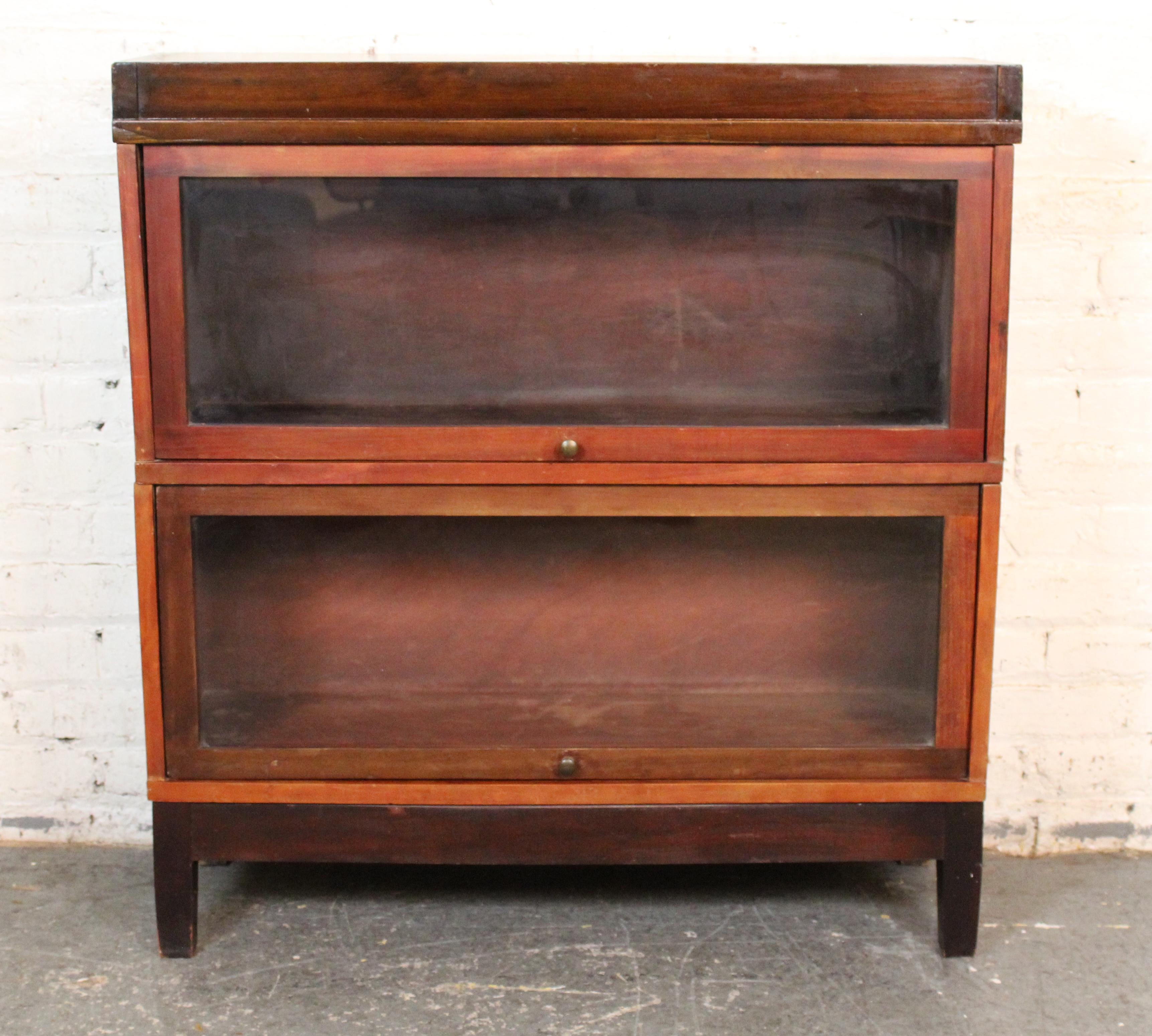 This two stack barrister bookcase made by Globe Wernicke in the early 1900s features their simple stacking design with separate base and topper. Both units have glass doors that open up-and-in. The glass front doors protect your books or valuables