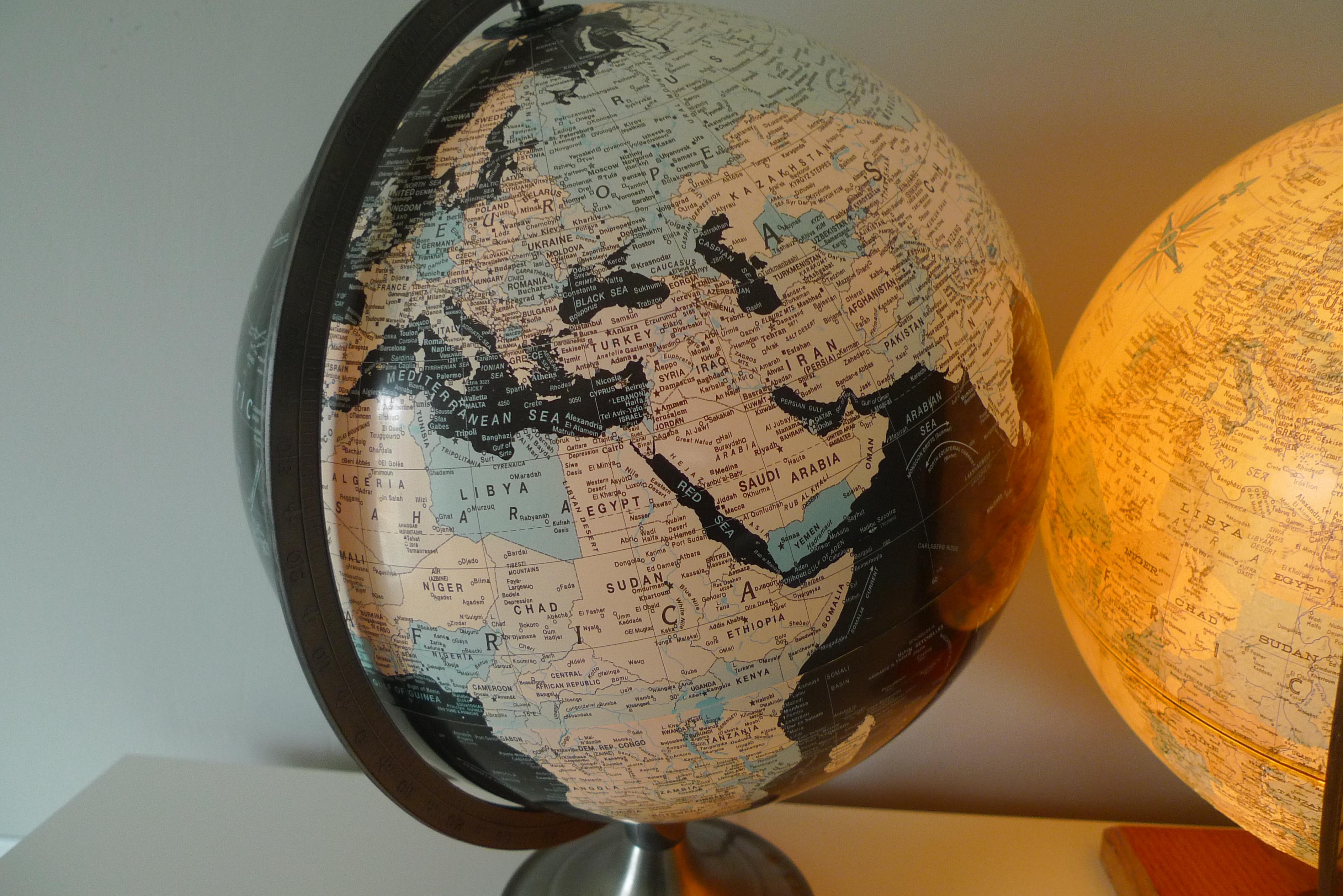 Pair of illuminated globes from Replogle. The darker colored globe is a Scan Globe with population centers delineated. Its stand is circular steel. The lighter colored globe is from the Premier Series and has raised topographical highlights. Its
