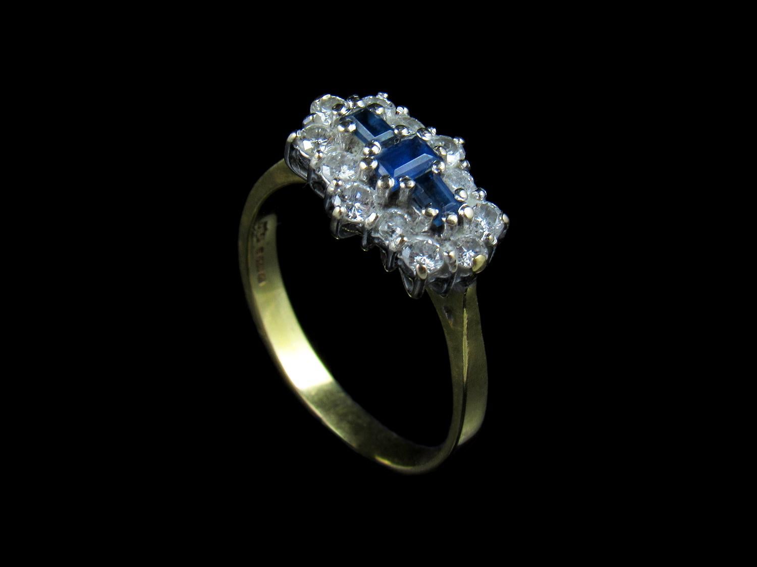 A beautiful sapphire and diamond ring.

In the centre are three baguette cut strong and bright blue sapphires (one 3mm x 4mm and two 3mm x 2mm) encircled by ten crystal clear round brilliant cut diamonds. All the gemstones are original and are