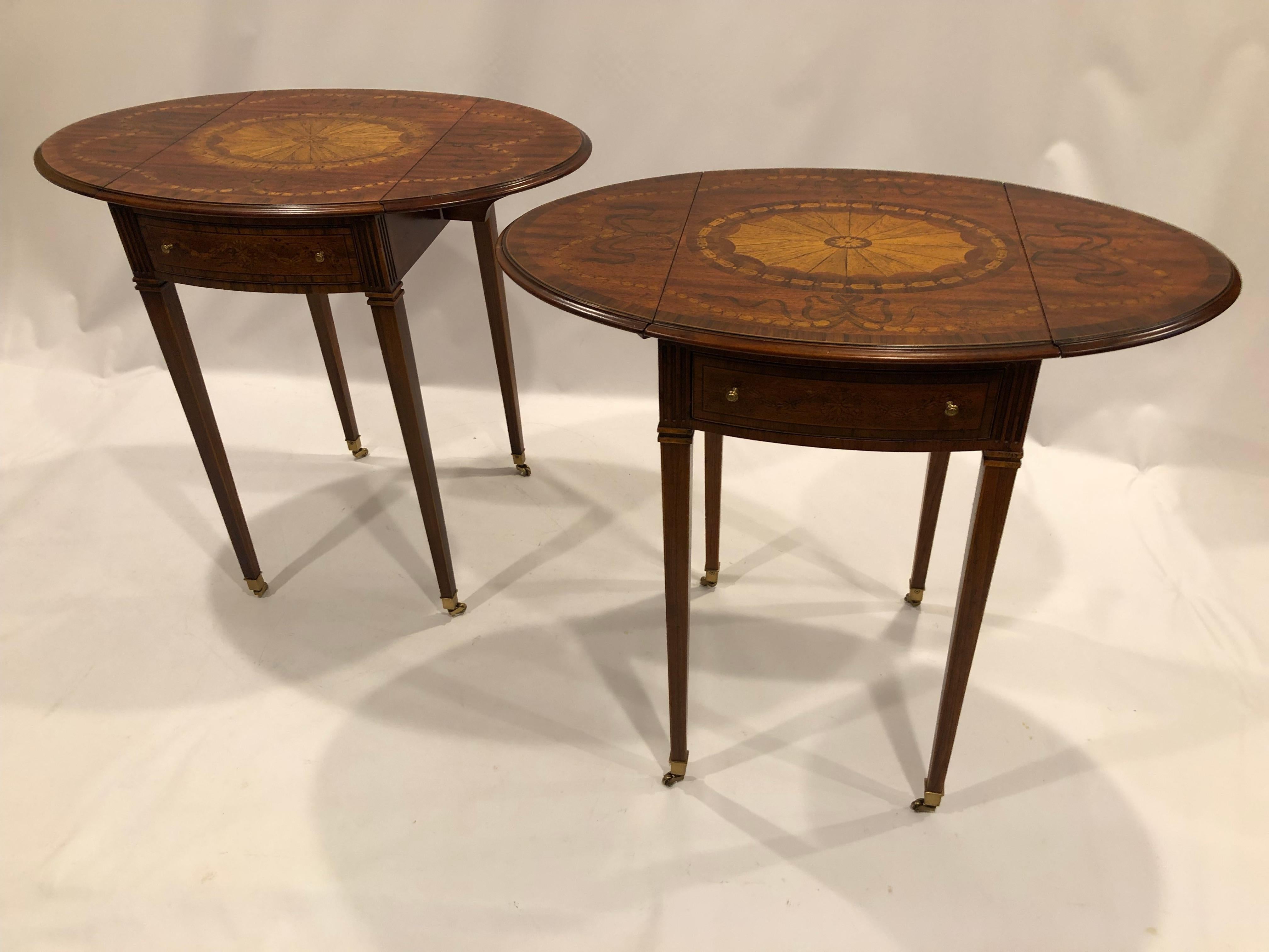 Magnificent pair of inlaid mixed wood drop leaf end tables that measure 15.25 w and are rectangular with the leaves down; 30.5 w and oval when open. There is one working drawer in each, and a faux drawer en verso. The central medallions vary