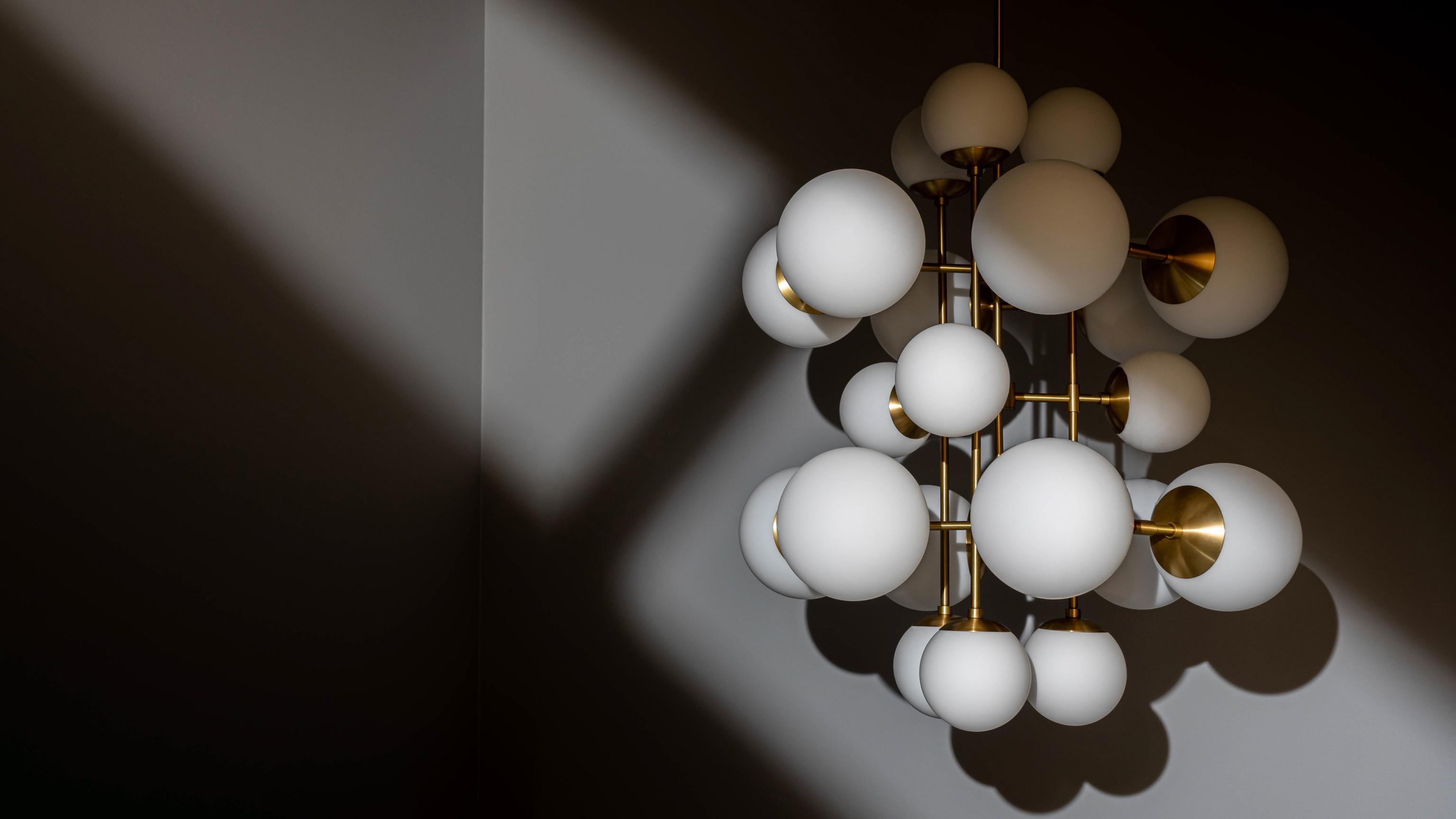 A kaleidoscope of glass spheres perambulates around a linear brass frame. Made with two sizes of glass globes, available in three types of signature glass, the shifting symmetries and enchanting interplay of configurations create changing patterns