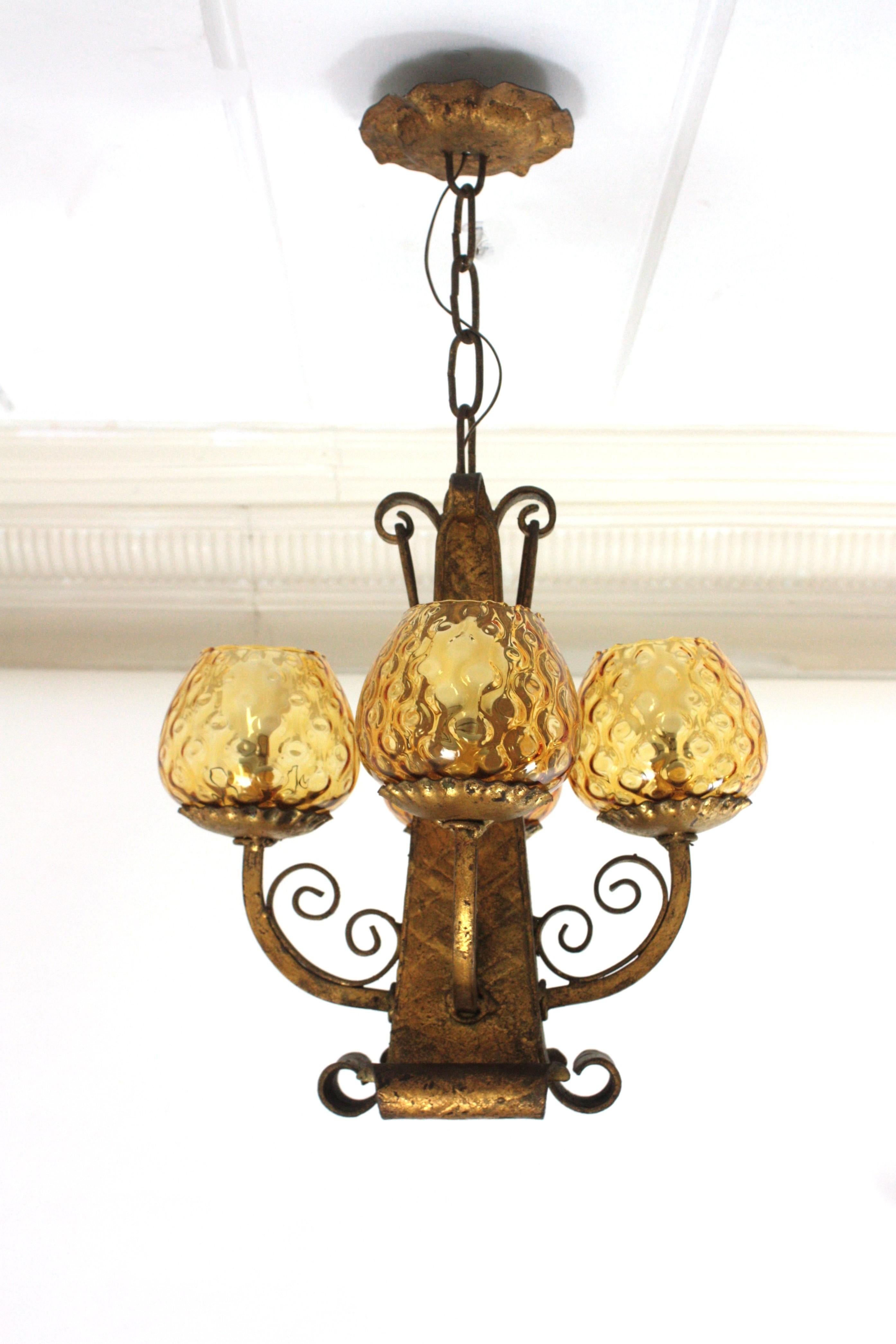 Lustre à quatre branches en fer doré forgé à la main et verre ambré
Espagne, années 1940.
Suspension ou plafonnier à quatre lumières en fer forgé à la main avec abat-jour en forme de globe ambré
Ce lustre accrocheur est doté d'une structure conique