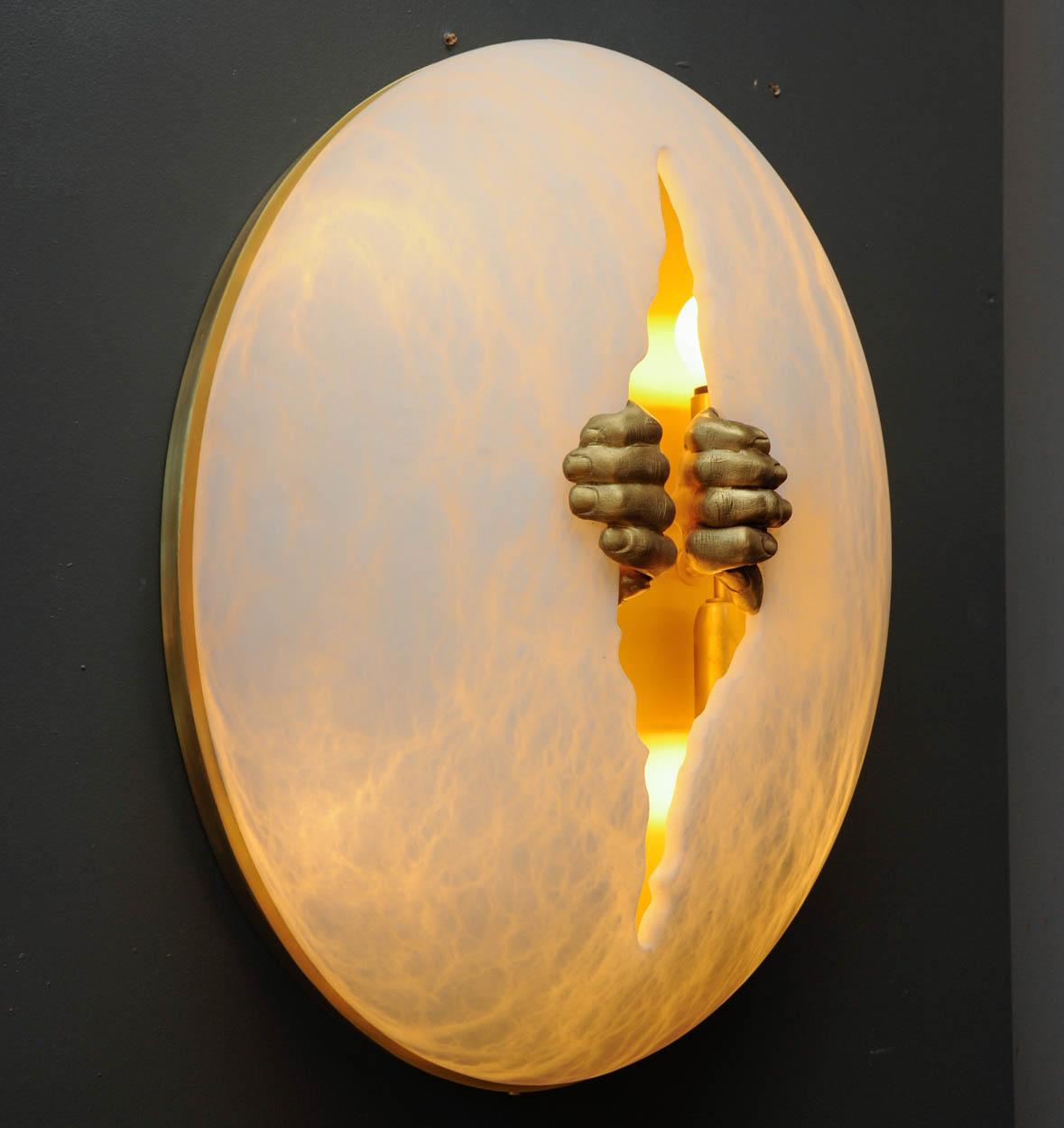 New exclusive design by Glustin Luminaires, egg shaped alabaster sconce with a crack carved in the middle spread by a pair of brass hands. Satin brass plate on the back.
Two lights inside the sconce.