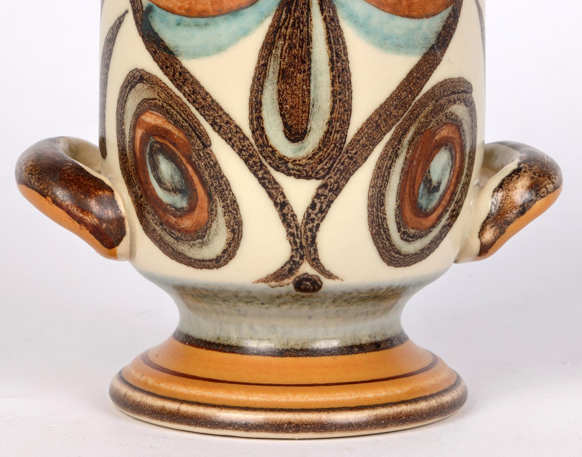 Un élégant vase à deux anses en grès de Langley Pottery, décoré du motif Soraya de Glyn Colledge (Britannique, 1922-2000) et datant des années 1970. Le vase, de facture robuste, repose sur un piédestal rond et un corps de forme cylindrique, avec des