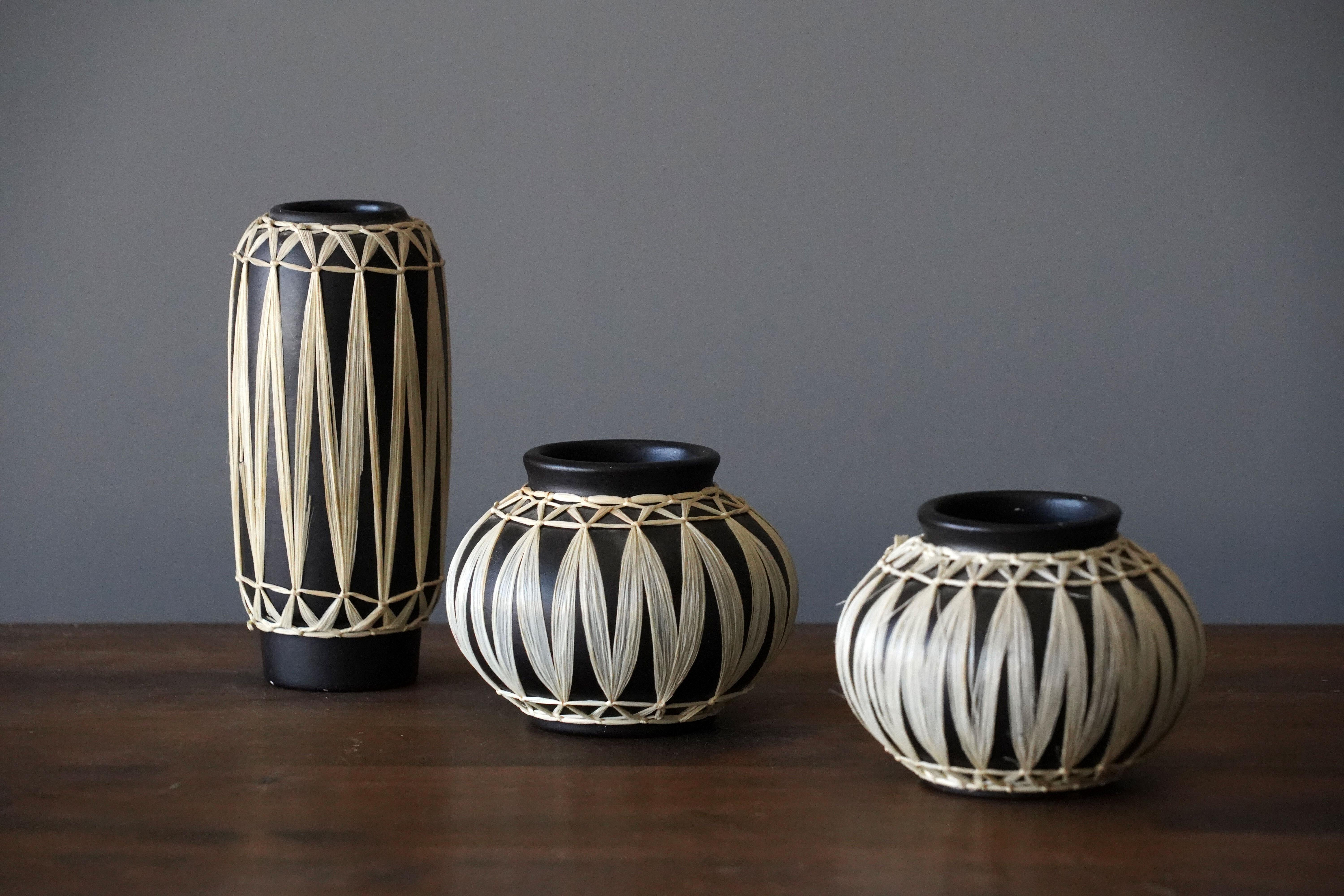 A set of small vases by Gmundner Keramik. In black painted stoneware, wrapped in raffia. Marked.

Stated dimensions are of the tall vase.