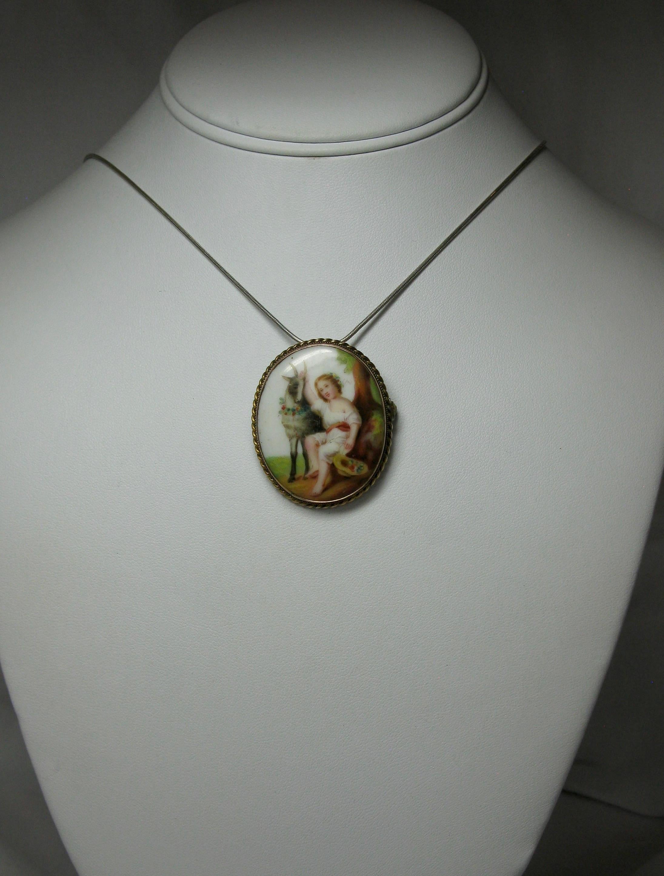 A stunning antique Victorian Pendant Brooch with a romantic hand painted image of a child and goat.  The goat with a garland of flowers around its neck.  The child with flowers in the hair and flowers on the hat.  The two friends rest in a bucolic